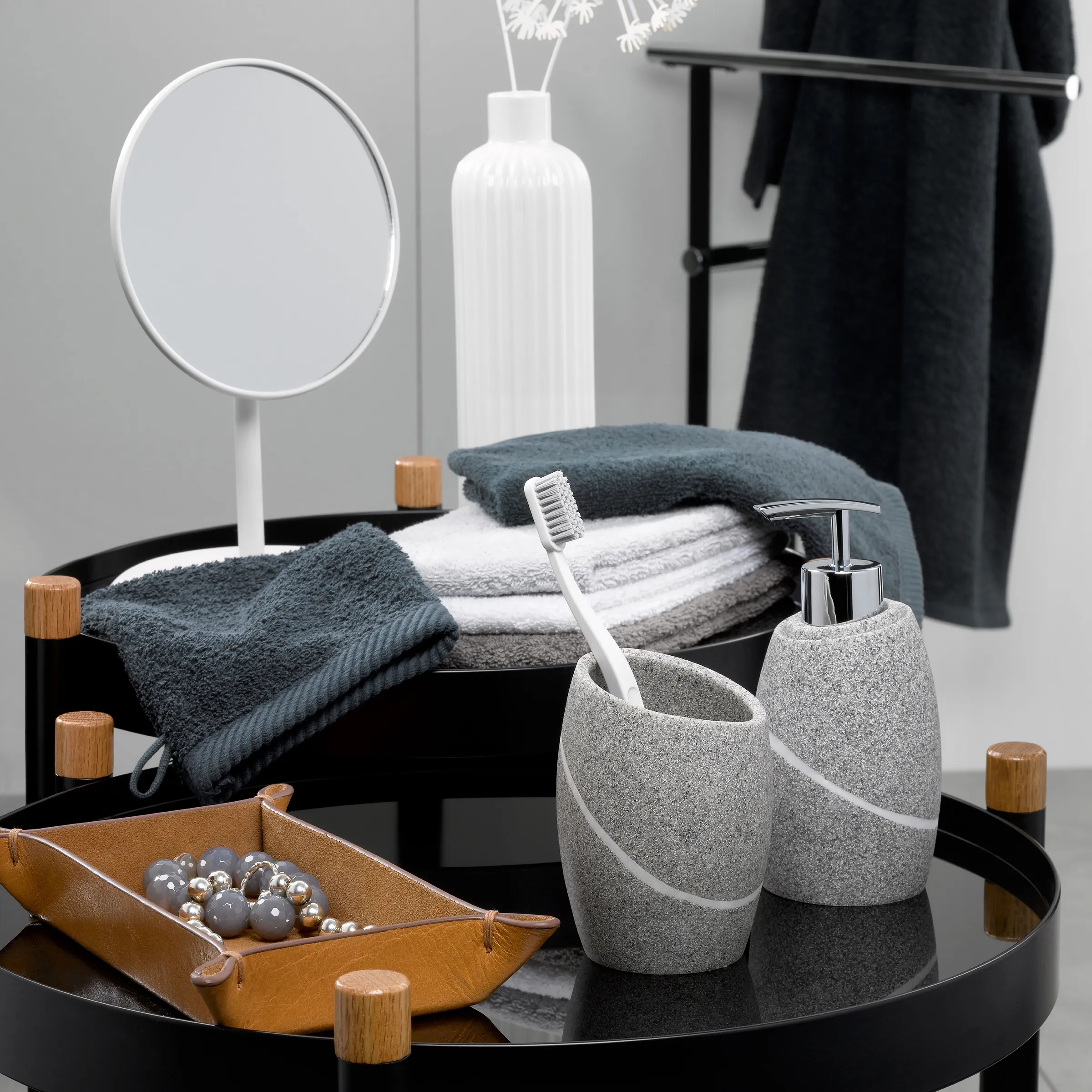 Badezimmer-Accessoire-Set mit Spiegel und Handtüchern - Moderne Baddekoration Modernes Badezimmer-Set mit Spiegel, Handtüchern, Zahnbürstenhalter, Seifenspender und Deko auf schwarzen Tabletts