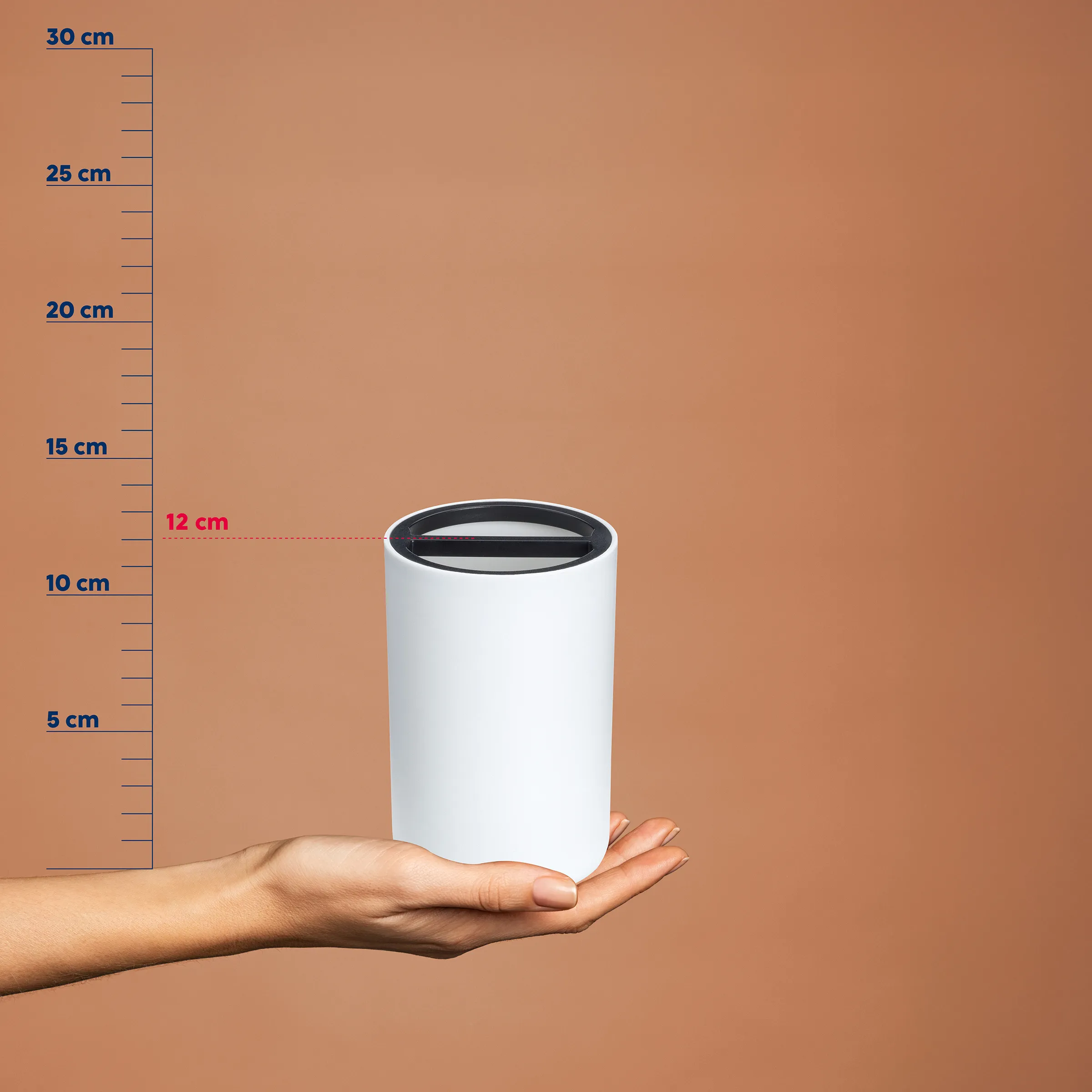 Weiße Spardose Zylinder - Kompakte Sparbüchse Weiße zylindrische Spardose mit schwarzem Schlitz auf einer Hand, neben einer Messskala von 0-30 cm. Höhe etwa 12 cm.