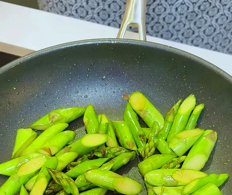 Grüner Spargel in der Pfanne braten - Gesunde Gemüsezubereitung Grüner Spargel wird in einer beschichteten Pfanne mit goldenem Griff angebraten
