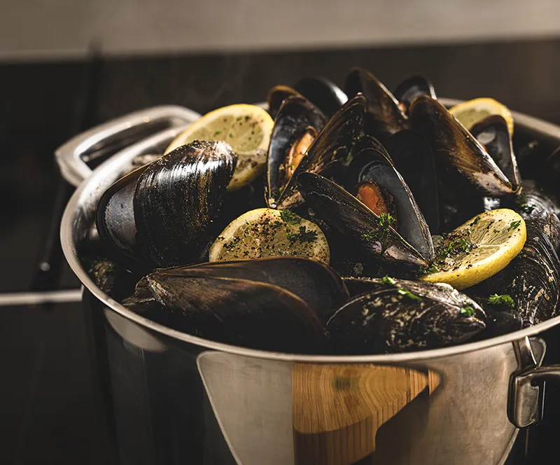Gekochte Muscheln Rezept - Frische Meeresfrüchte zubereiten Topf mit gekochten schwarzen Muscheln, Zitronenscheiben und Petersilie auf dunklem Hintergrund
