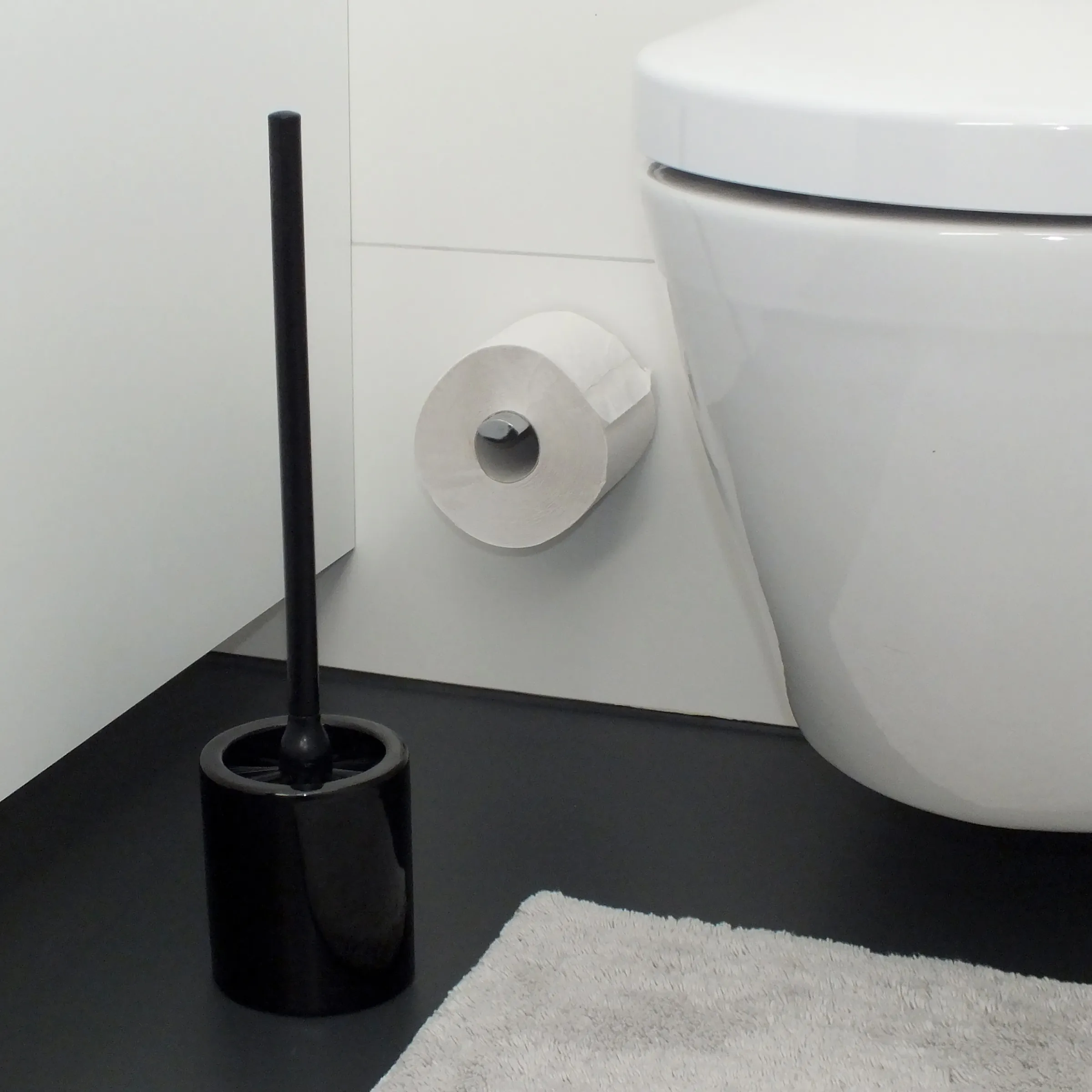 Badezimmer-Set mit schwarzer Toilettenbürste, weißem Toilettenpapierhalter und weißer Toilette auf schwarzem Boden