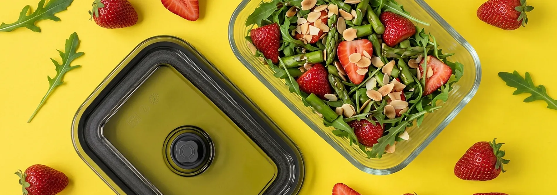 Vakuumbehälter für frische Salate - Meal Prep mit Erdbeeren und Spargel Vakuumbehälter und Frühlingssalat mit Erdbeeren, Spargel, Rucola und Mandeln auf gelbem Hintergrund