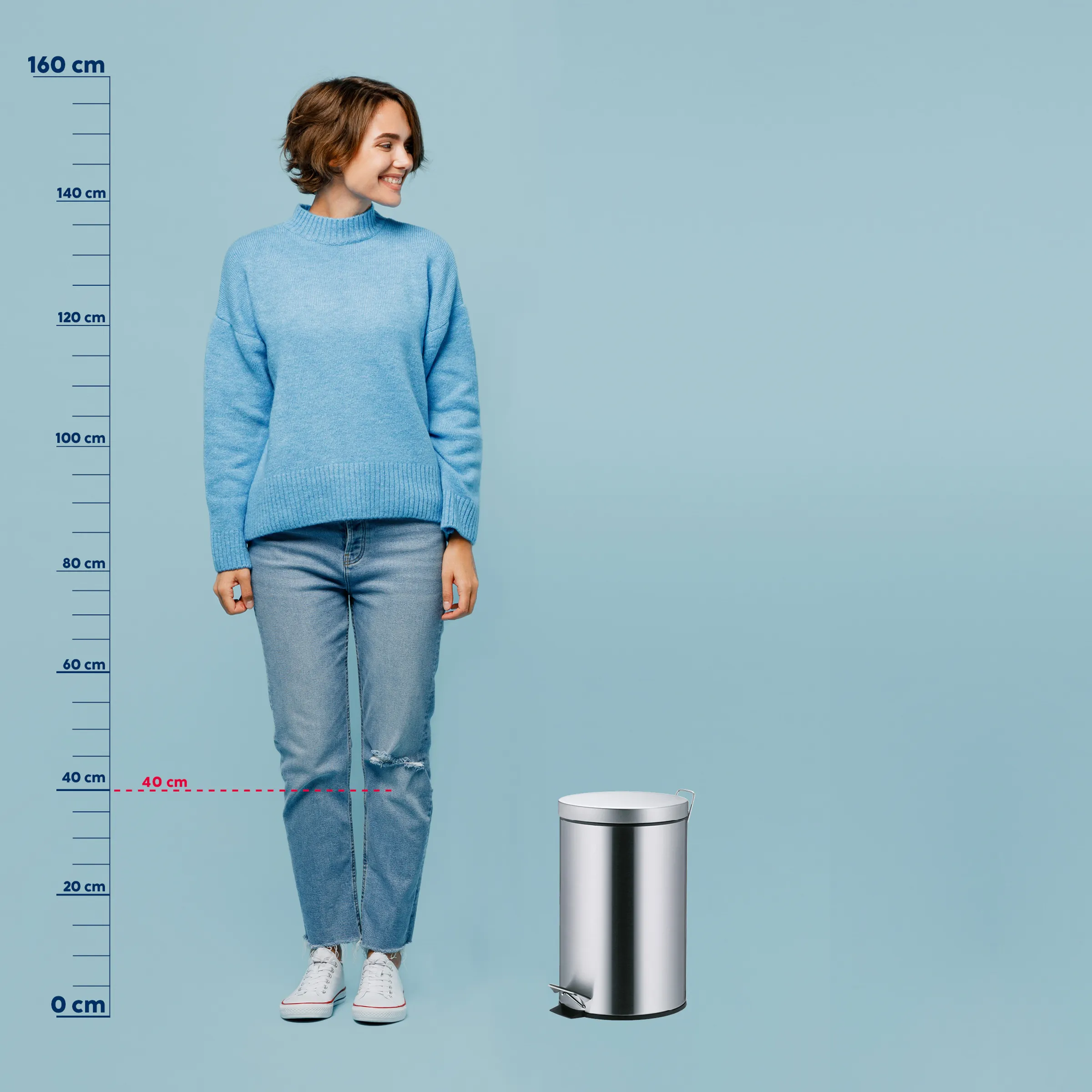 Mülleimer Größenvergleich - Edelstahl Treteimer Junge Frau in blauem Pullover und Jeans steht neben silbernem Mülleimer mit Größenvergleich-Skala