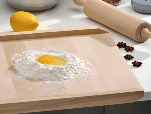 Teigzubereitung mit Mehl und Ei - Backen und Kochen Zutaten auf Holzbrett Mehl mit Ei in der Mitte auf Holzbrett, Nudelholz und Zitrone im Hintergrund für Teigzubereitung