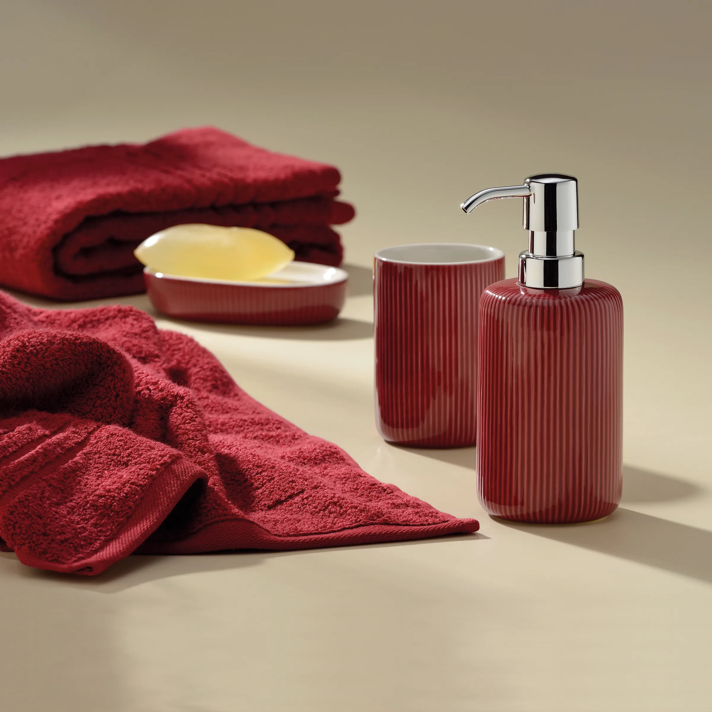 Badezimmer-Accessoires Set in Rot mit Seifenspender und Handtüchern Rotes Badezimmer-Set mit gerilltem Seifenspender, Becher und Seifenschale, dekoriert mit bordeauxfarbenen Handtüchern