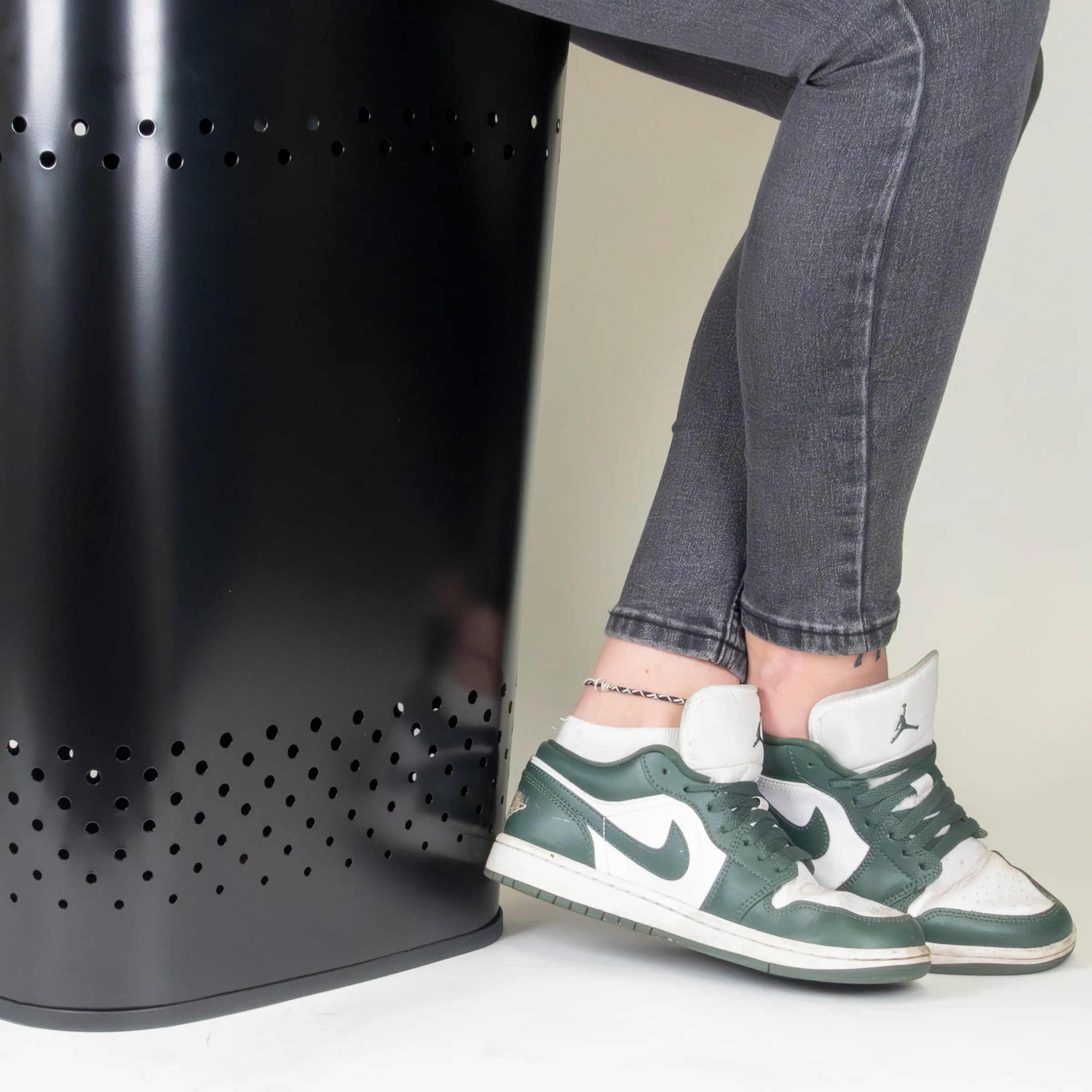 Person in grauer Jeans mit grün-weißen Jordan Sneakers neben schwarzem Metallhocker mit Lochdesign