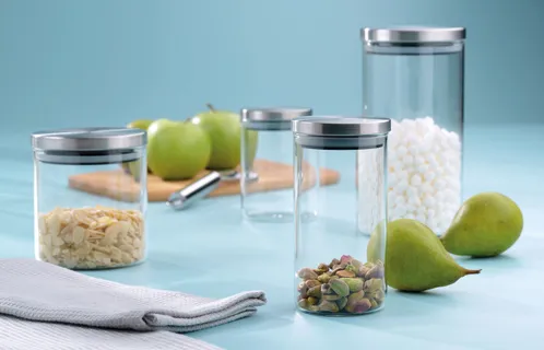 Glas-Vorratsdosen mit Deckel - Küchen-Aufbewahrung für Lebensmittel Glas-Vorratsdosen mit Metalldeckel gefüllt mit Müsli und Nüssen, daneben grüne Birnen auf weißer Oberfläche