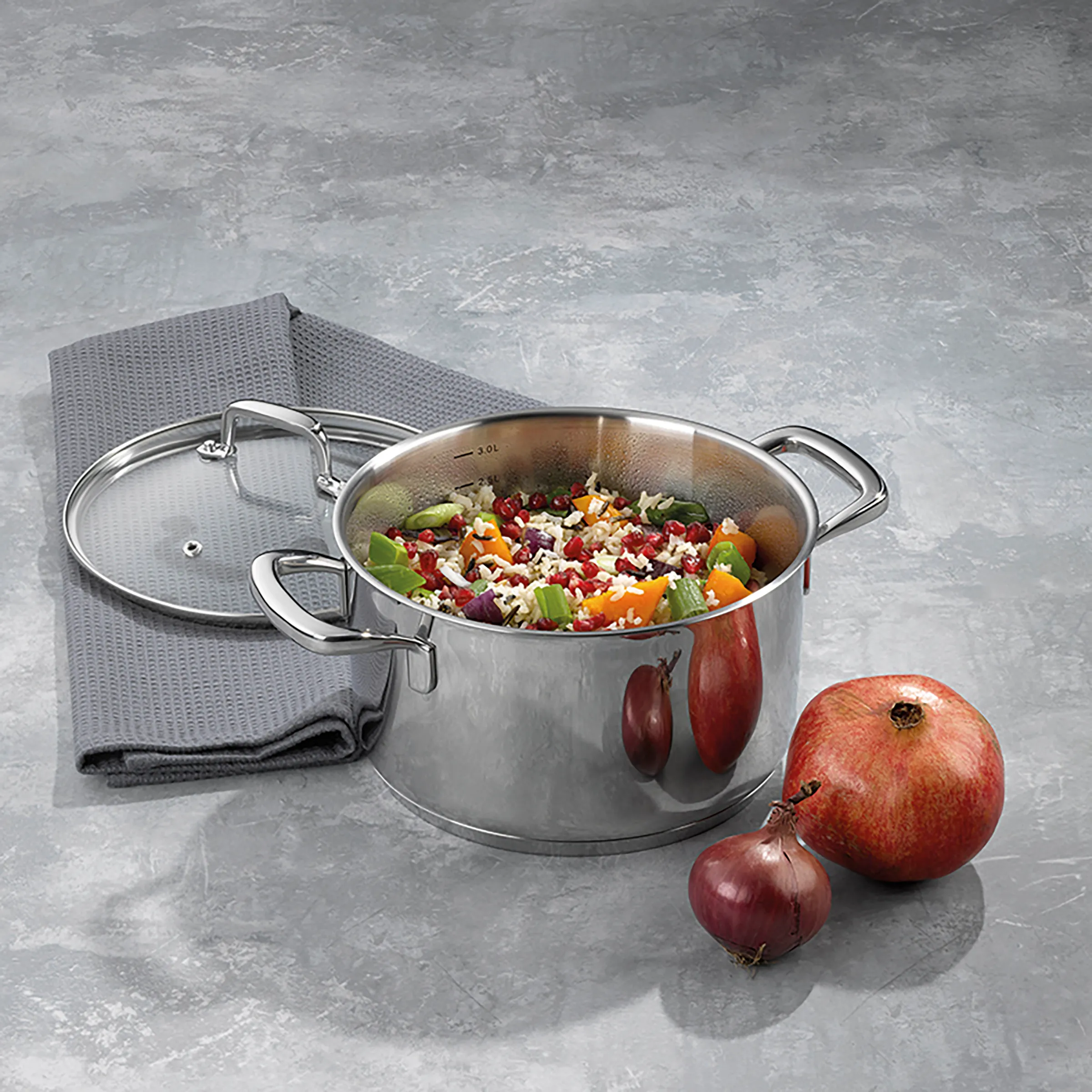Edelstahl-Kochtopf mit Glasdeckel und Gemüse – Hochwertige Kochgeschirr Edelstahl-Kochtopf mit Glasdeckel gefüllt mit buntem Gemüsesalat, daneben Granatapfel und rote Zwiebeln