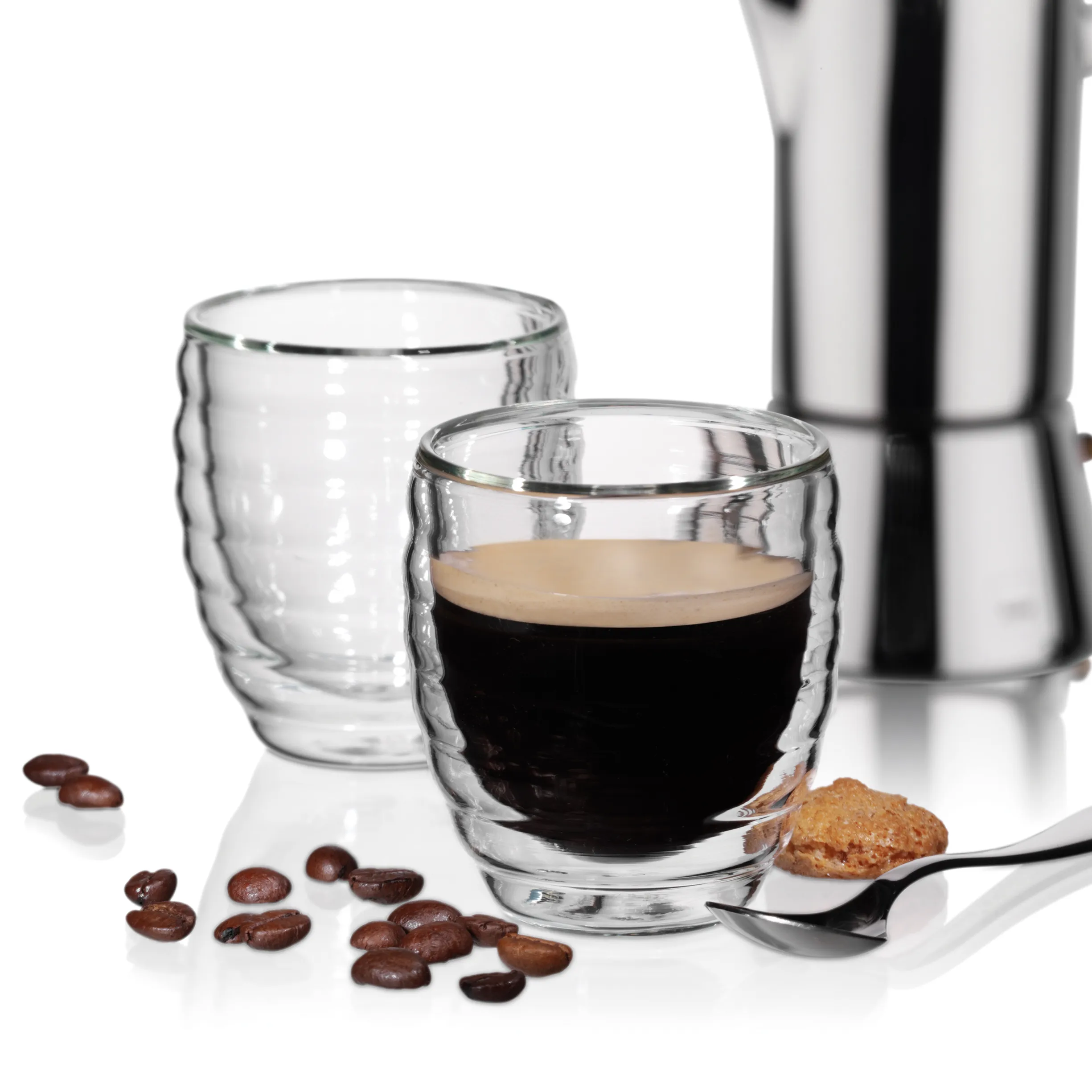 Doppelwandige Glastassen für Espresso und Kaffee Zwei doppelwandige Glastassen mit Espresso und Kaffeekörnern, daneben eine Metallkanne und ein Keks auf weißem Hintergrund