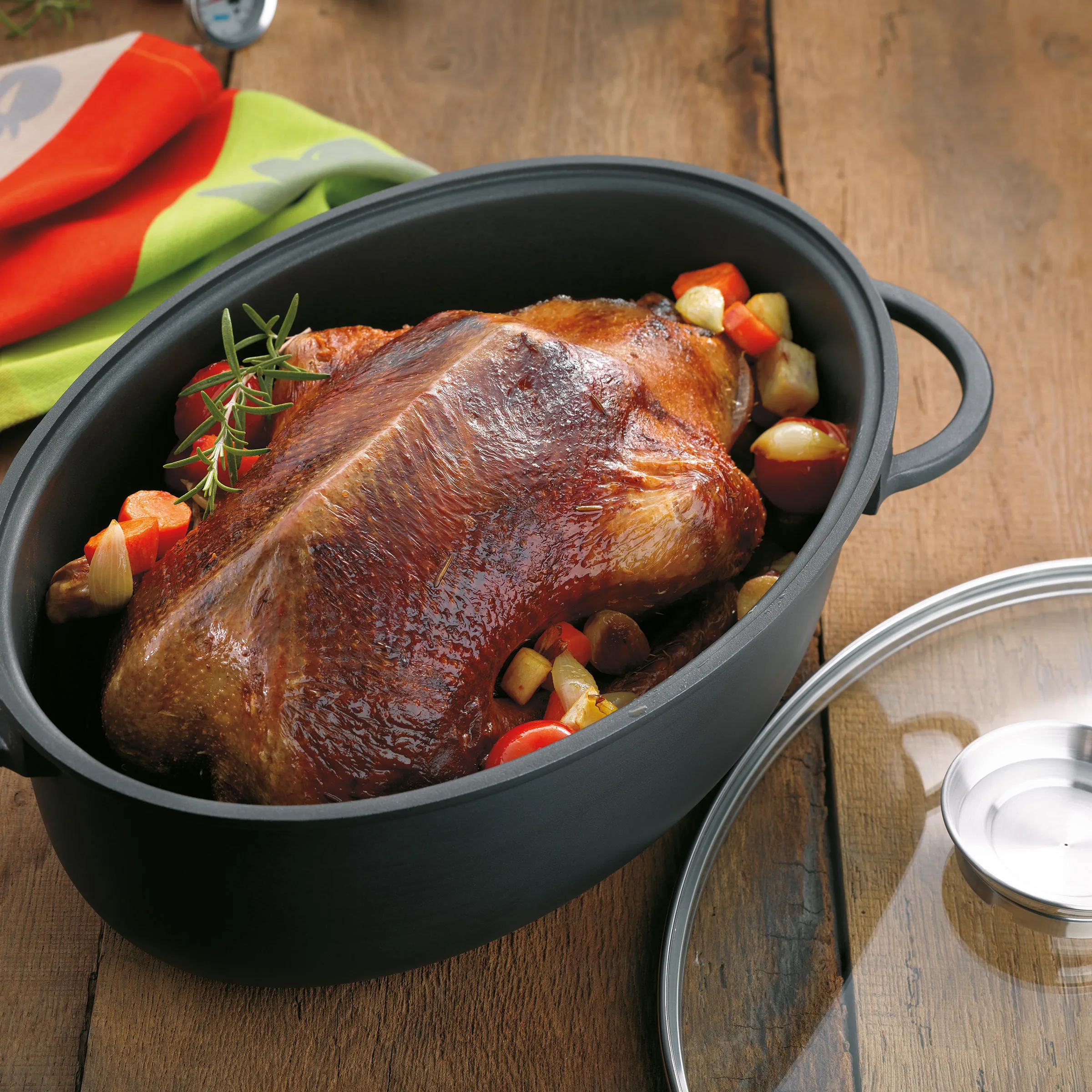 Brathähnchen Rezept: Saftiges Hähnchen im Bräter Gebratenes Hähnchen in schwarzem Bräter mit Rosmarin, Kartoffeln und Gemüse auf Holztisch
