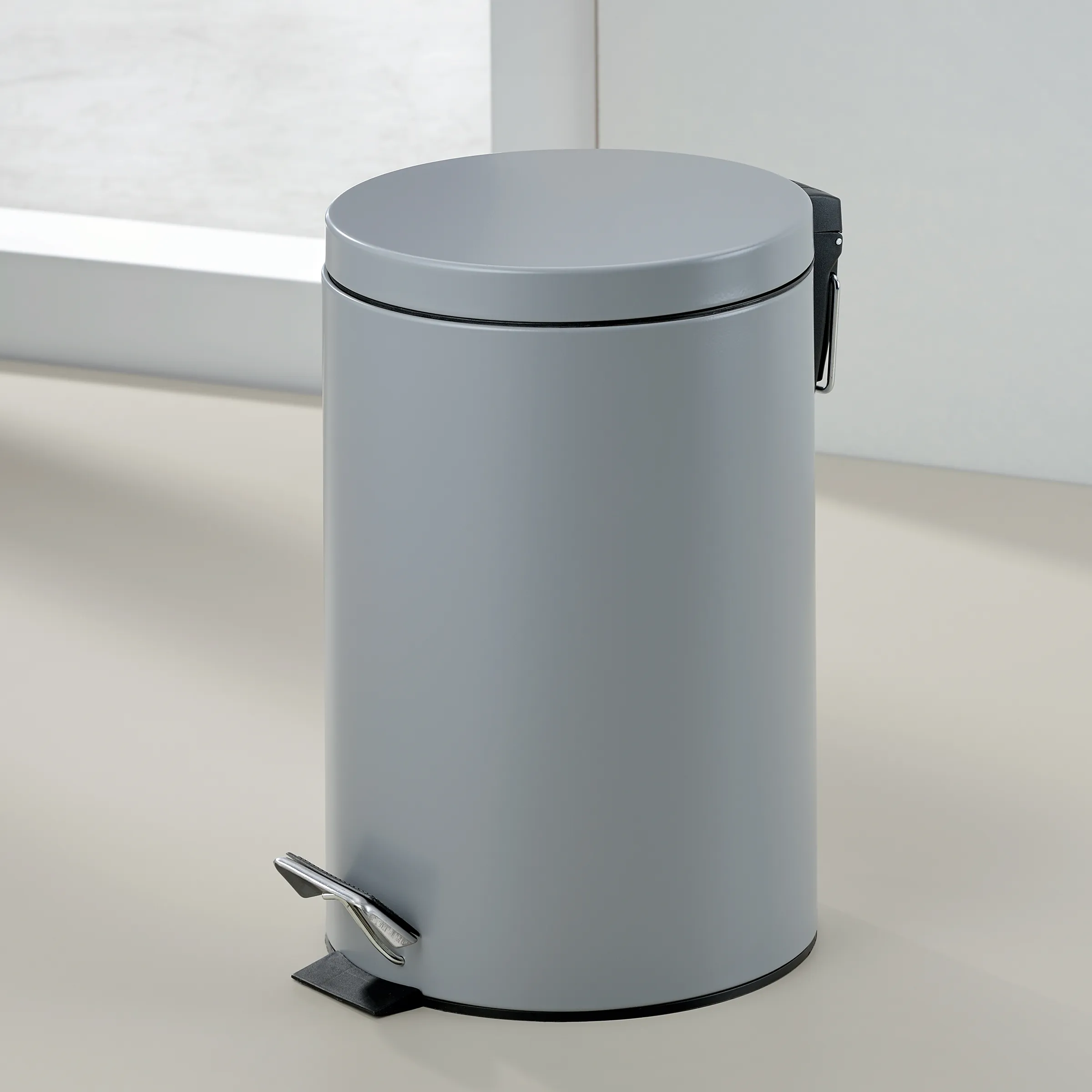 Grauer Tretmülleimer mit Pedal - moderner runder Abfalleimer Grauer runder Tretmülleimer mit Deckel und Fußpedal, modernes minimalistisches Design auf hellem Boden
