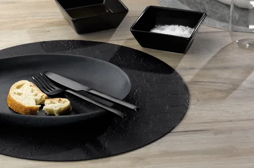 Elegantes Geschirr Set - schwarze Teller mit Besteck Modernes Tischgedeck mit schwarzem Teller, Besteck und Serviette auf Holztisch mit Gewürzbehältern