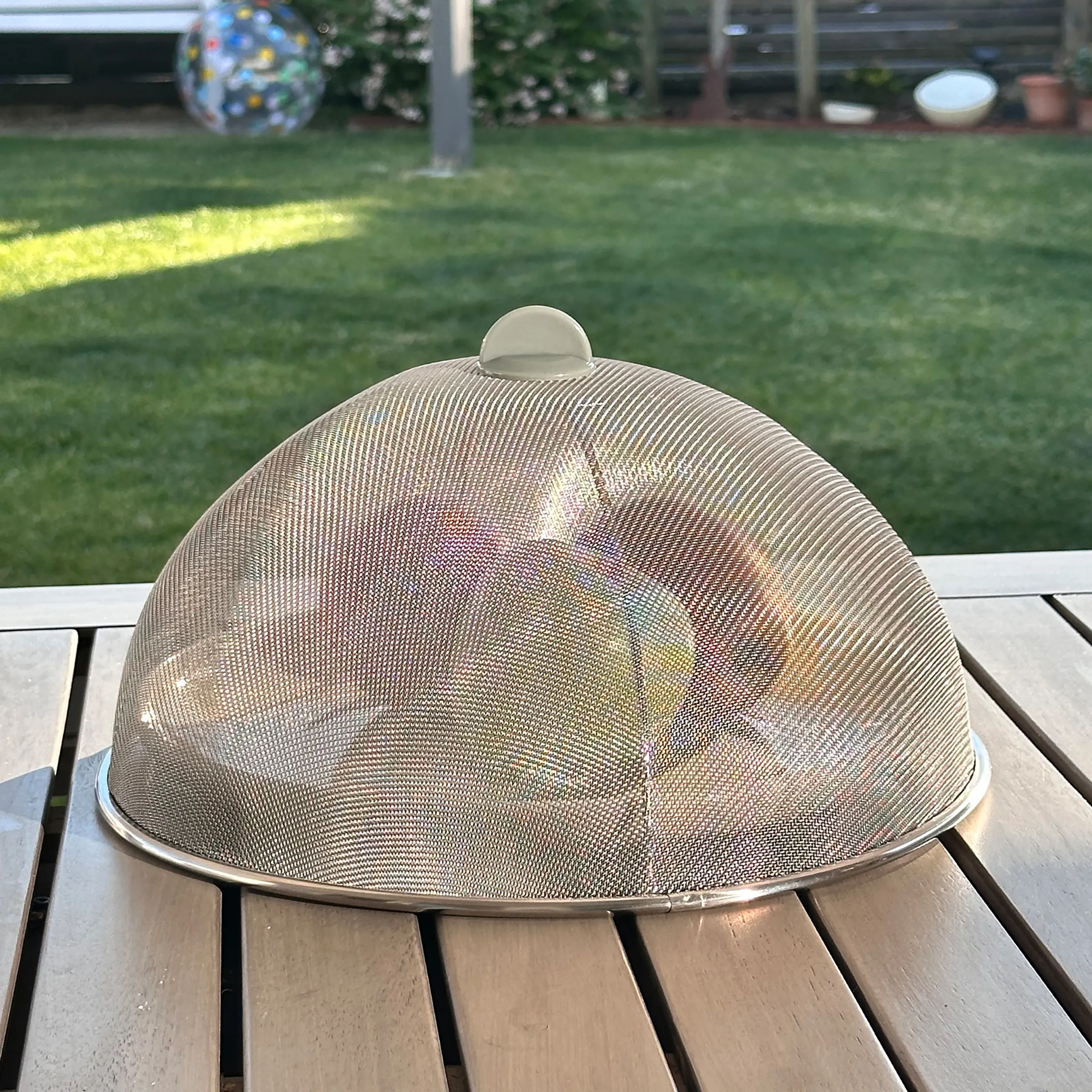 Metallische Fliegenhaube aus Edelstahl-Gittergeflecht auf Holztisch im sonnigen Garten