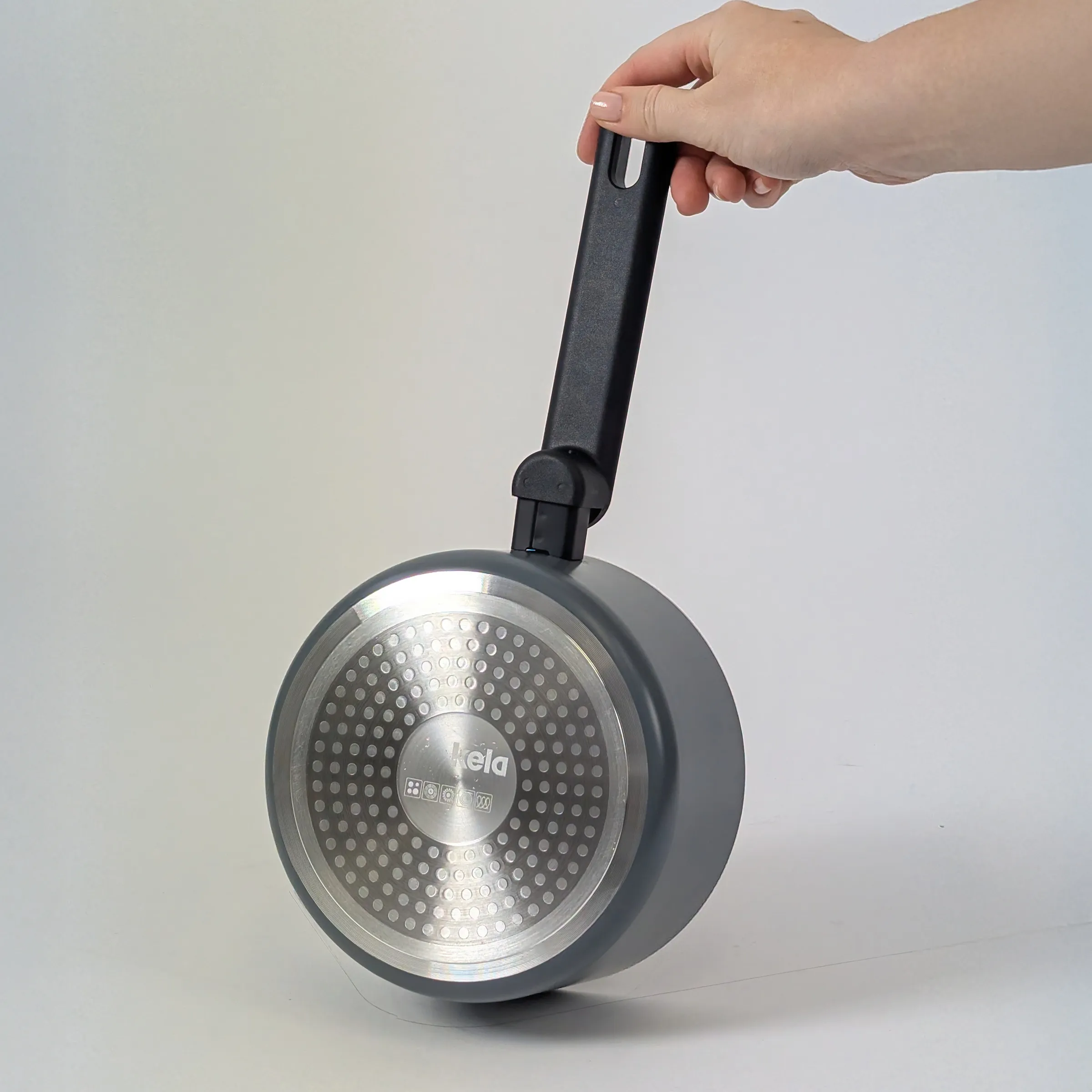 Tefal Bratpfanne mit Thermospot-Indikatior | Kochwerkzeug Hand hält schwarze Pfanne mit Edelstahl-Boden und Loch-Muster vor weißem Hintergrund