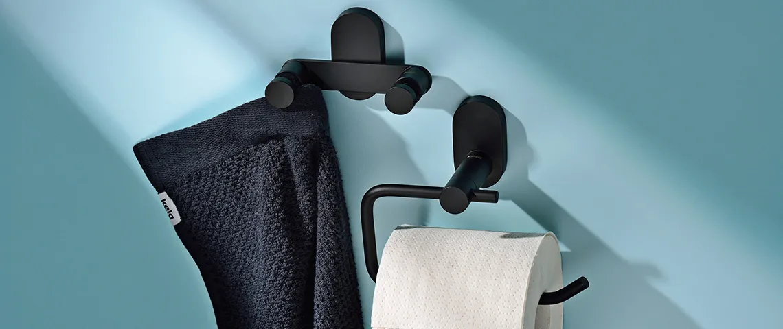 Schwarze Badezimmer-Wandhalterungen aus Metall halten ein dunkles Handtuch und eine weiße Toilettenpapierrolle an hellblauer Wand.
