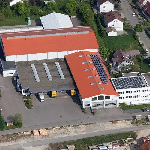 Industriegebäude Solarpanele Luftaufnahme Luftaufnahme eines Industriegebäudes mit rotem Dach, Solarpanelen und angrenzenden Wohnhäusern in grüner Umgebung.