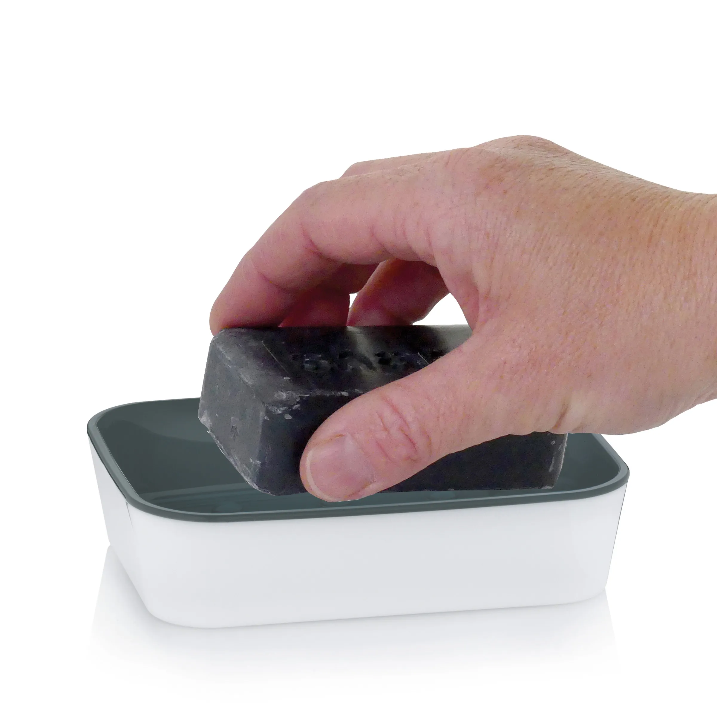Hand hält schwarze Seife über weißer Schale mit grünem Deckel zum Eintauchen