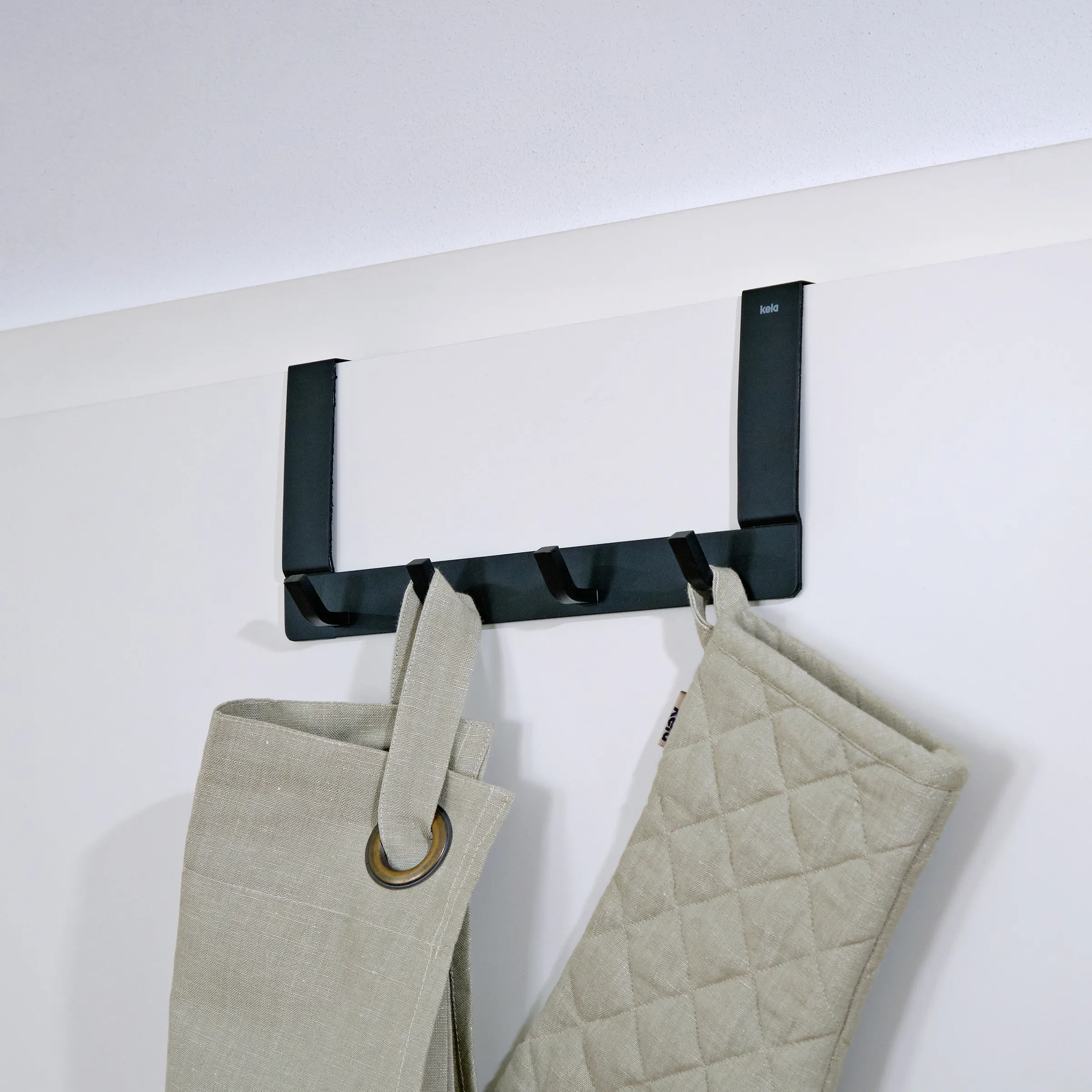 Wandgarderobe schwarz - Moderne Hakenleiste für Küche und Flur Schwarze Wandgarderobe mit zwei vertikalen Stangen und vier Haken, an denen cremefarbene Textilien hängen.