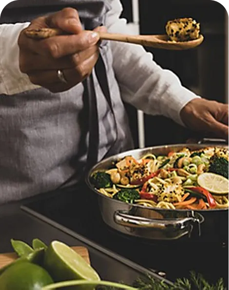 Wok Noodles Recipe - Asian Cuisine Cooking Person in gray apron serving wok noodles with vegetables and lime slices using a golden wok spatula