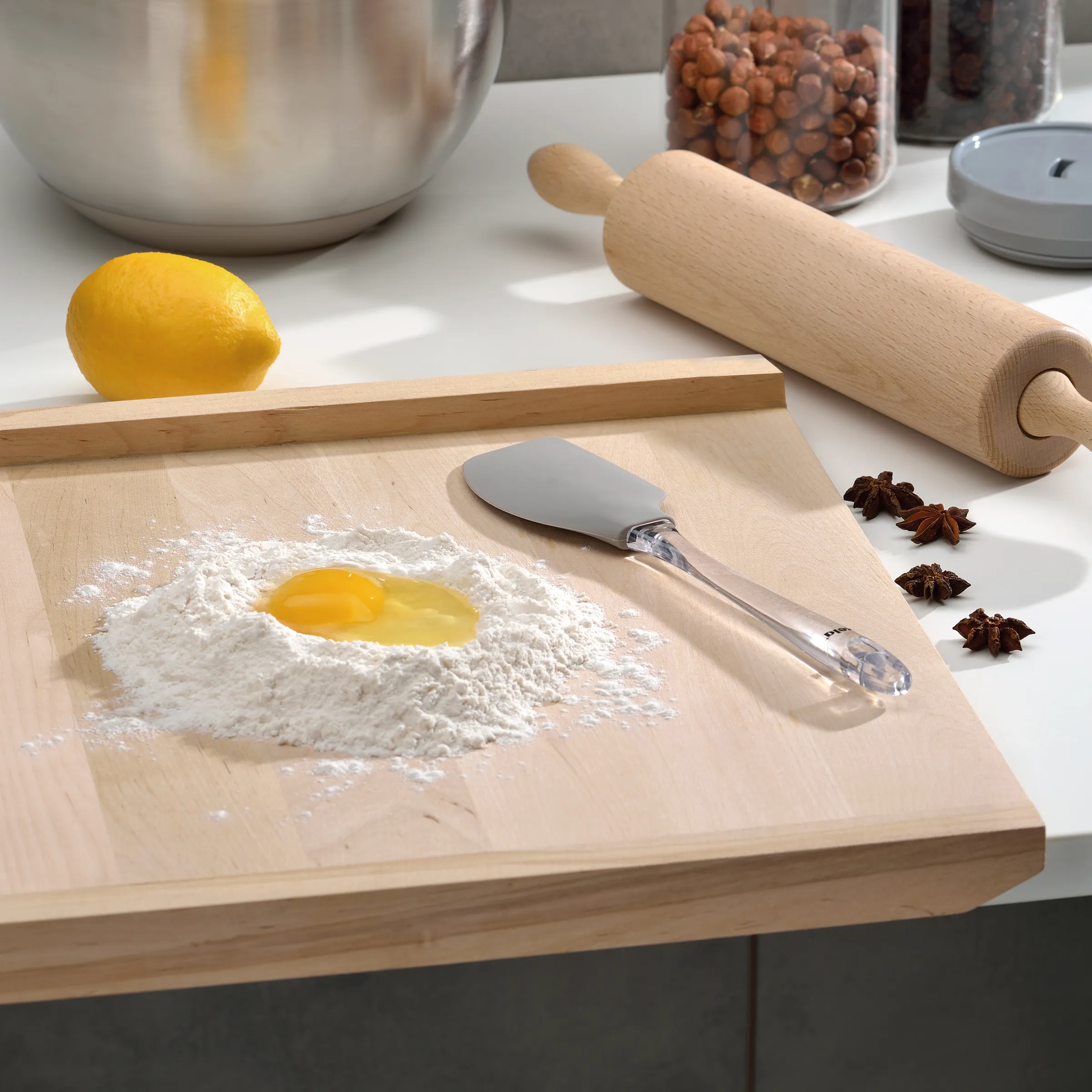 Backzutaten und Küchenwerkzeuge - Mehl, Ei und Nudelholz zum Backen Backzutaten auf Holzbrett: Mehl mit Ei, Nudelholz, Teigspatel, Zitrone, Sternanis und Haselnüsse im Hintergrund