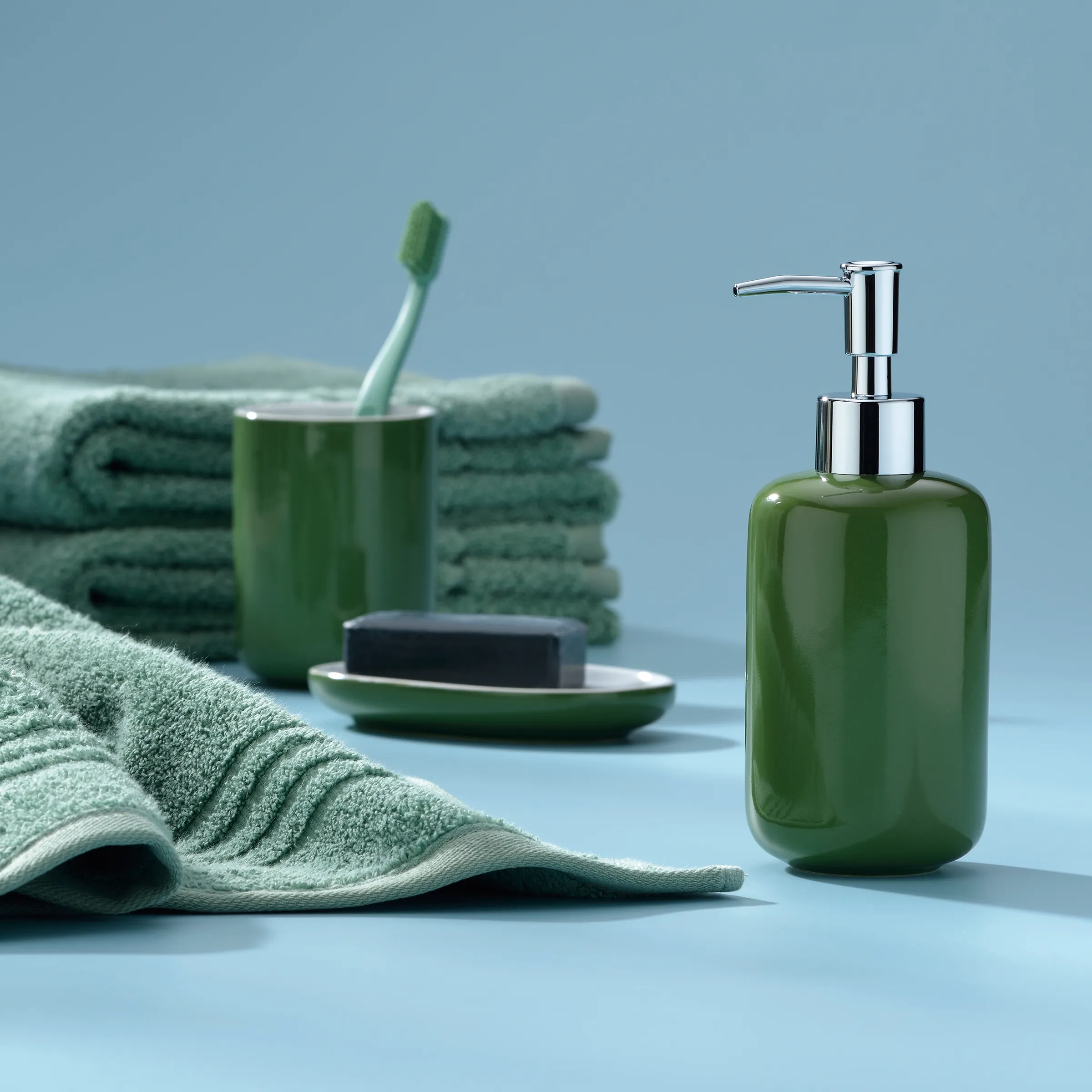 Grünes Badezimmer-Set mit Seifenspender, Zahnbürste, Handtüchern und Seife auf hellblauem Hintergrund