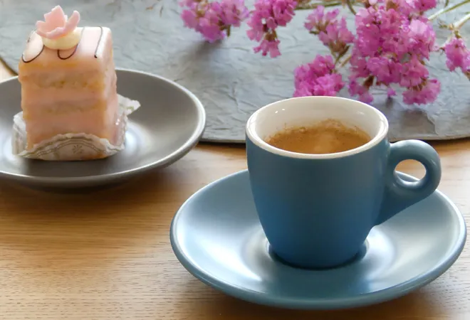 Tasse à Espresso Tasse à Café Bleue Tasse à espresso bleue sur soucoupe blanche remplie de café chaud, à côté d'une décoration de bougie rose et de fleurs magenta