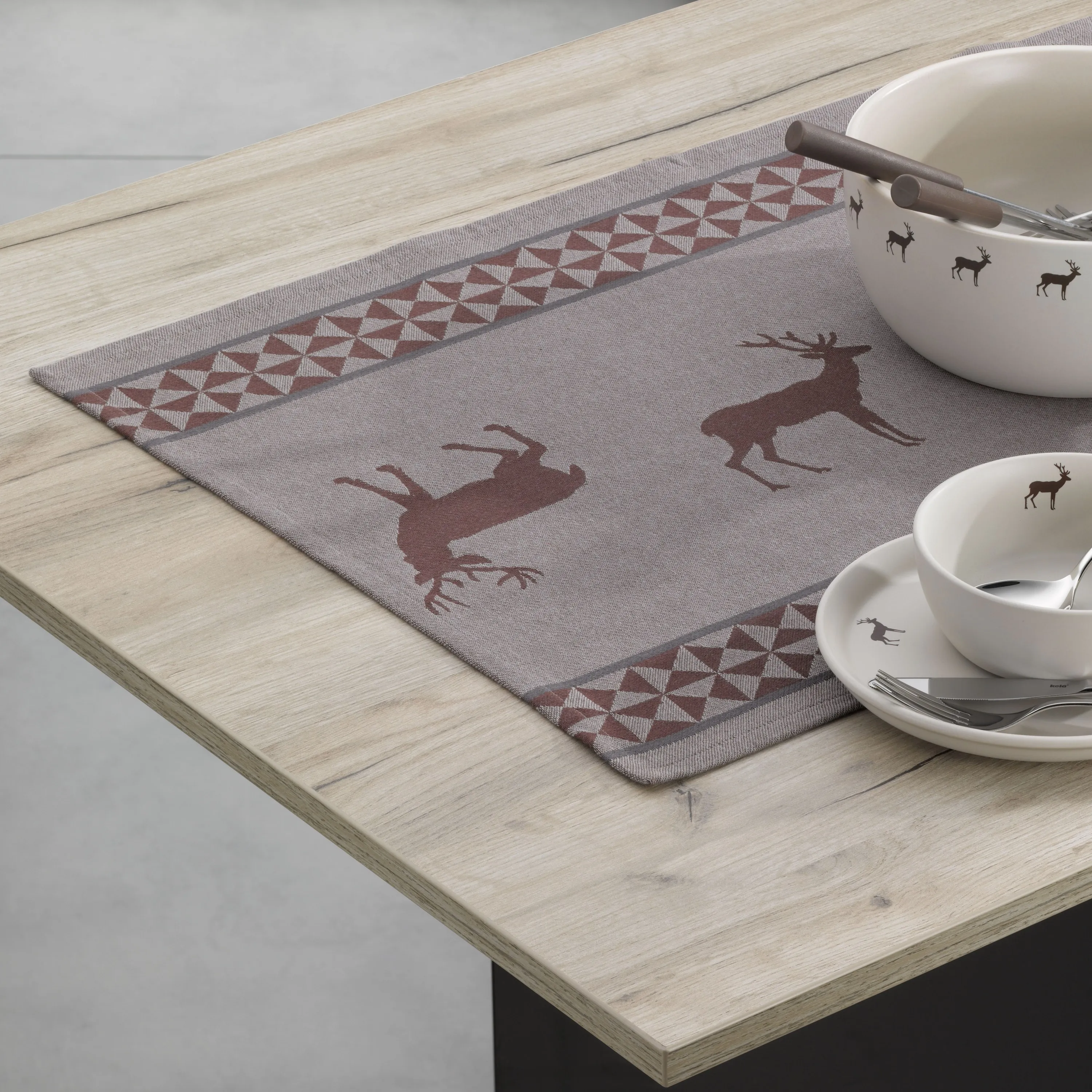 Tischset mit Hirsch-Motiv - elegante Tischdecke Grauer Tischset mit Hirsch-Motiv in Braun, geometrischem Muster und weißem Geschirr auf Holztisch