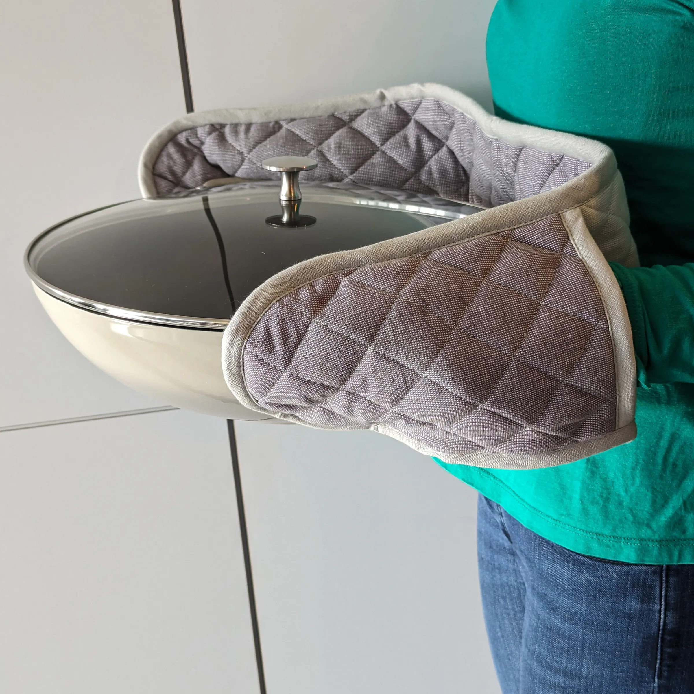 Hochwertige Topflappen Kochhandschuhe mit Wärmeschutz Quilted oven mitts in taupe held by person wearing turquoise shirt, displayed with cream pot lid