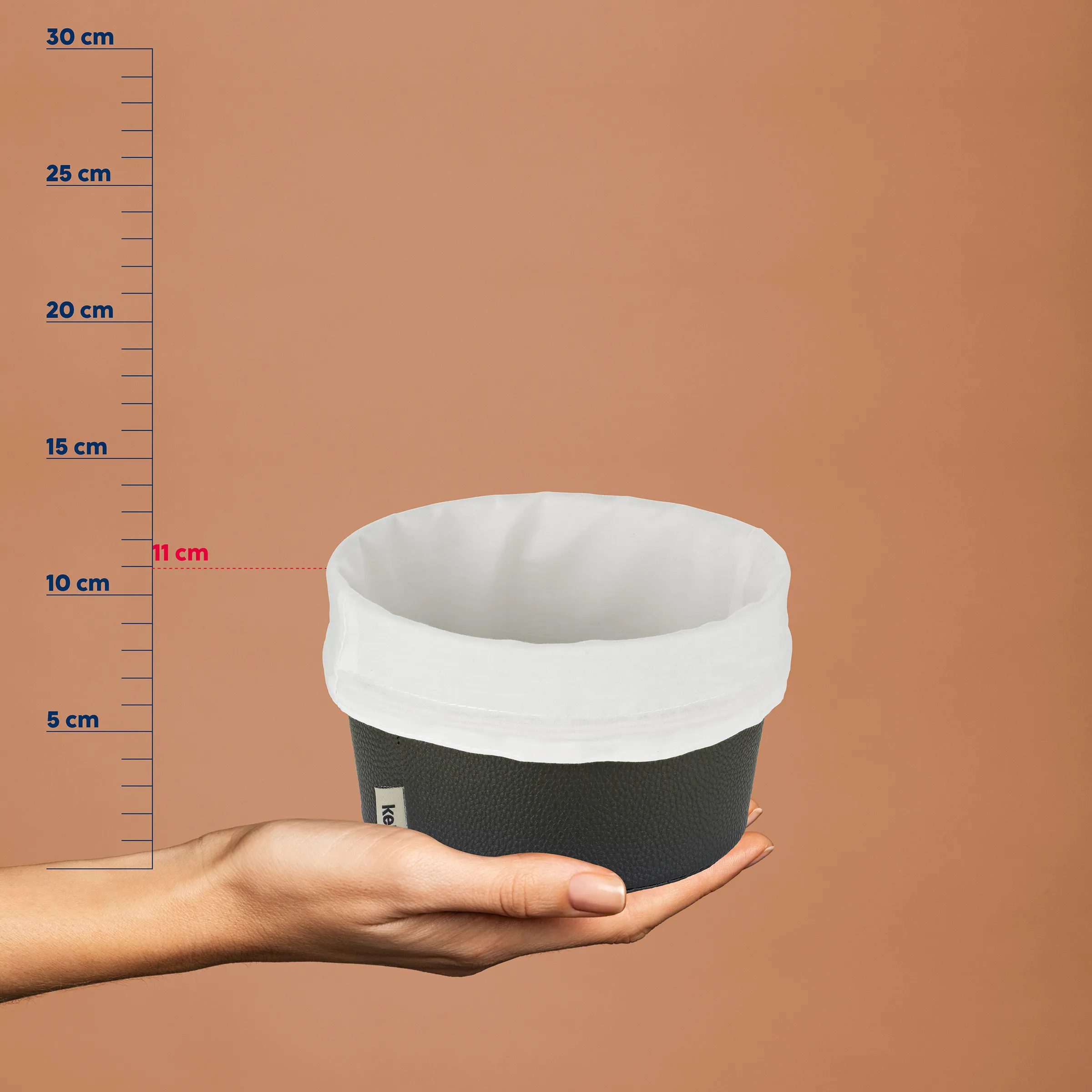 Wiederverwendbarer Kaffeebecher aus schwarzem Material mit weißem Deckel in einer Hand vor Maßstab