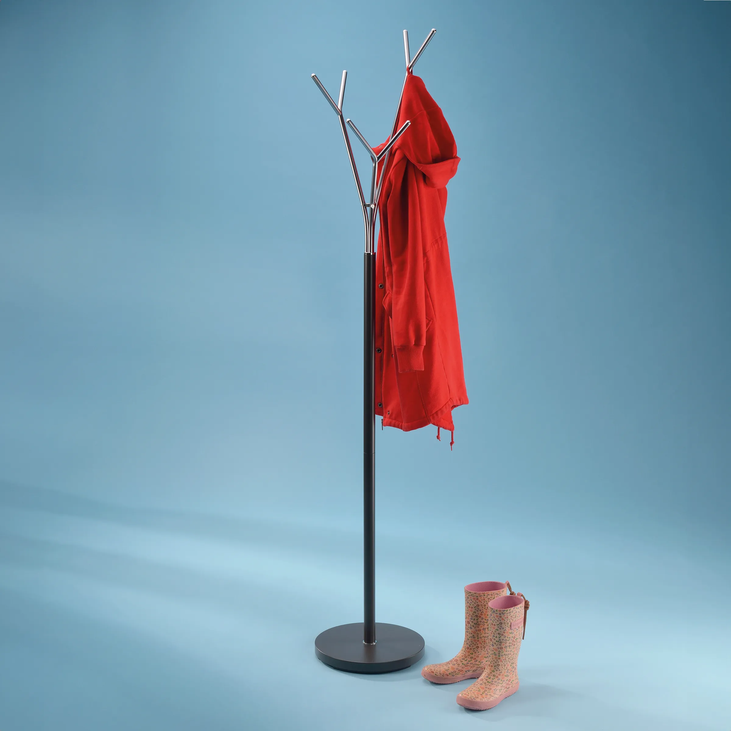 Moderner Garderobenständer aus Metall mit roter Regenjacke und rosa Gummistiefeln vor blauem Hintergrund