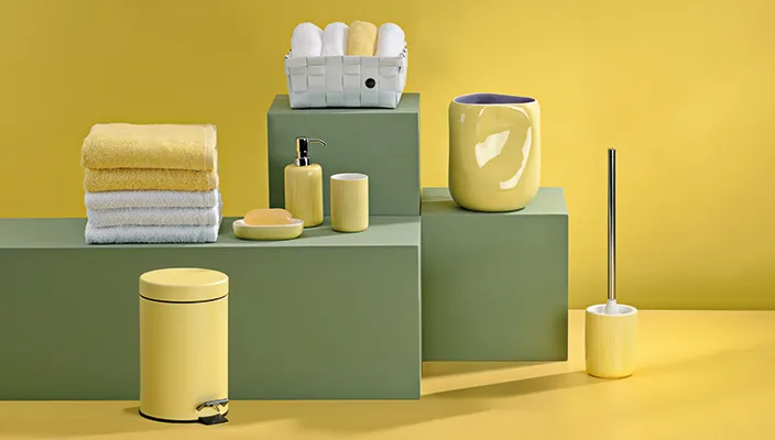 Badezimmer-Accessoires Set mit gelbem und grünem Design: Tücher, Seifenspender, Zahnbürstenhalter und Dekorelemente auf gestaffelten grünen Podesten vor gelbem Hintergrund.