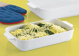 Nudelsalat Behälter - praktische Kunststoff-Schale Weiße Kunststoffschale mit Nudelsalat auf gelbem Untergrund, daneben blaue Ofenhandschuhe