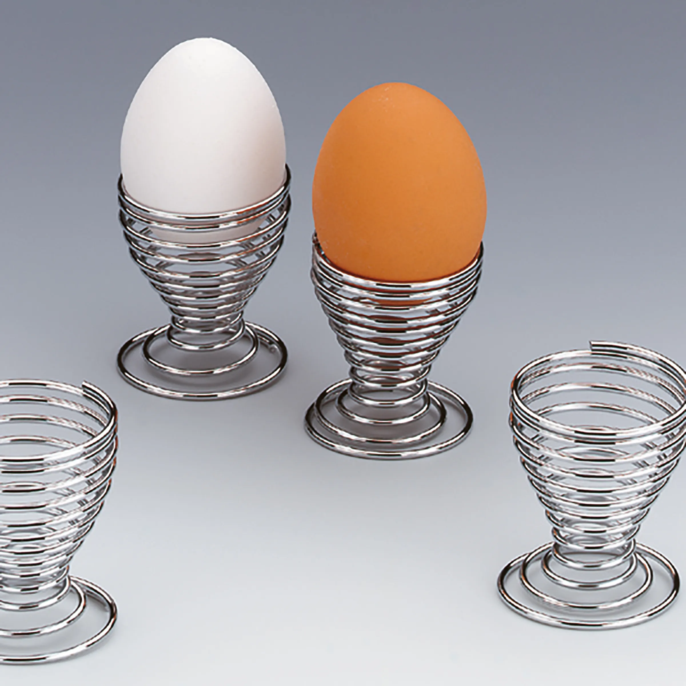 Eierbecher Glas Metall Set - Frühstücksgeschirr Vier Eierbecher aus Glas und Metall mit weißem und braunem Ei, auf grauem Hintergrund