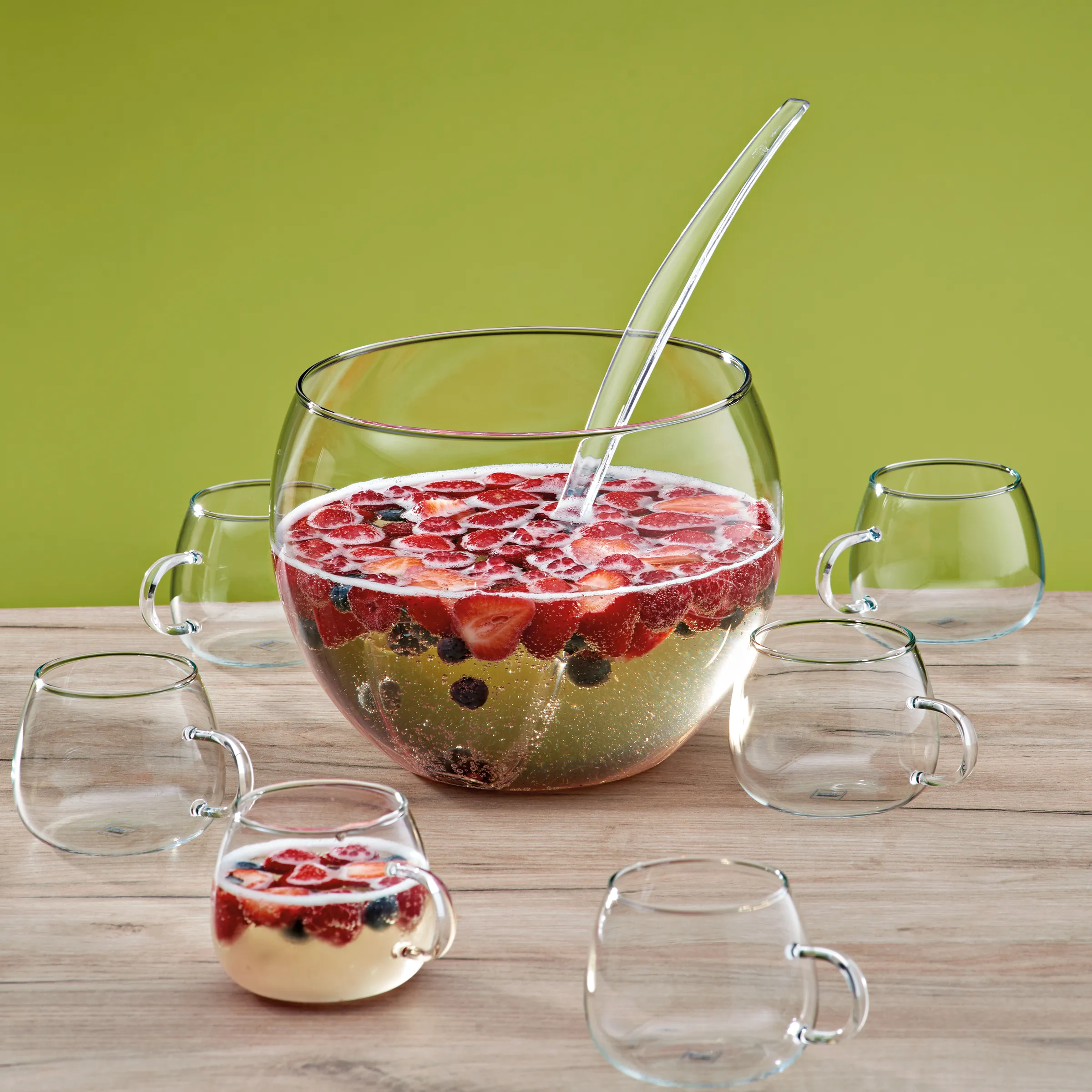 Glas-Bowle-Set mit Schöpfkelle und Punsch-Gläsern für Fruchtbowle Glas-Bowle-Set mit Früchtepunsch, Erdbeeren und Beeren, umgeben von kleinen Gläsern mit Henkel