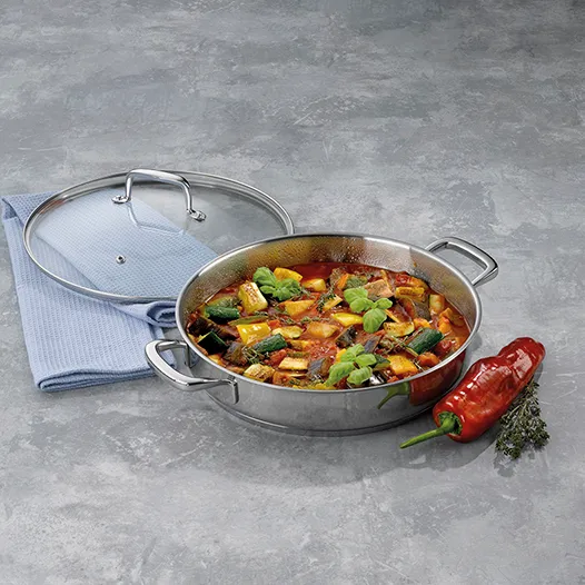Edelstahl-Kochtopf mit buntem Gemüse-Eintopf, Glasdeckel, Kochlöffel und rote Chilischote auf grauem Untergrund