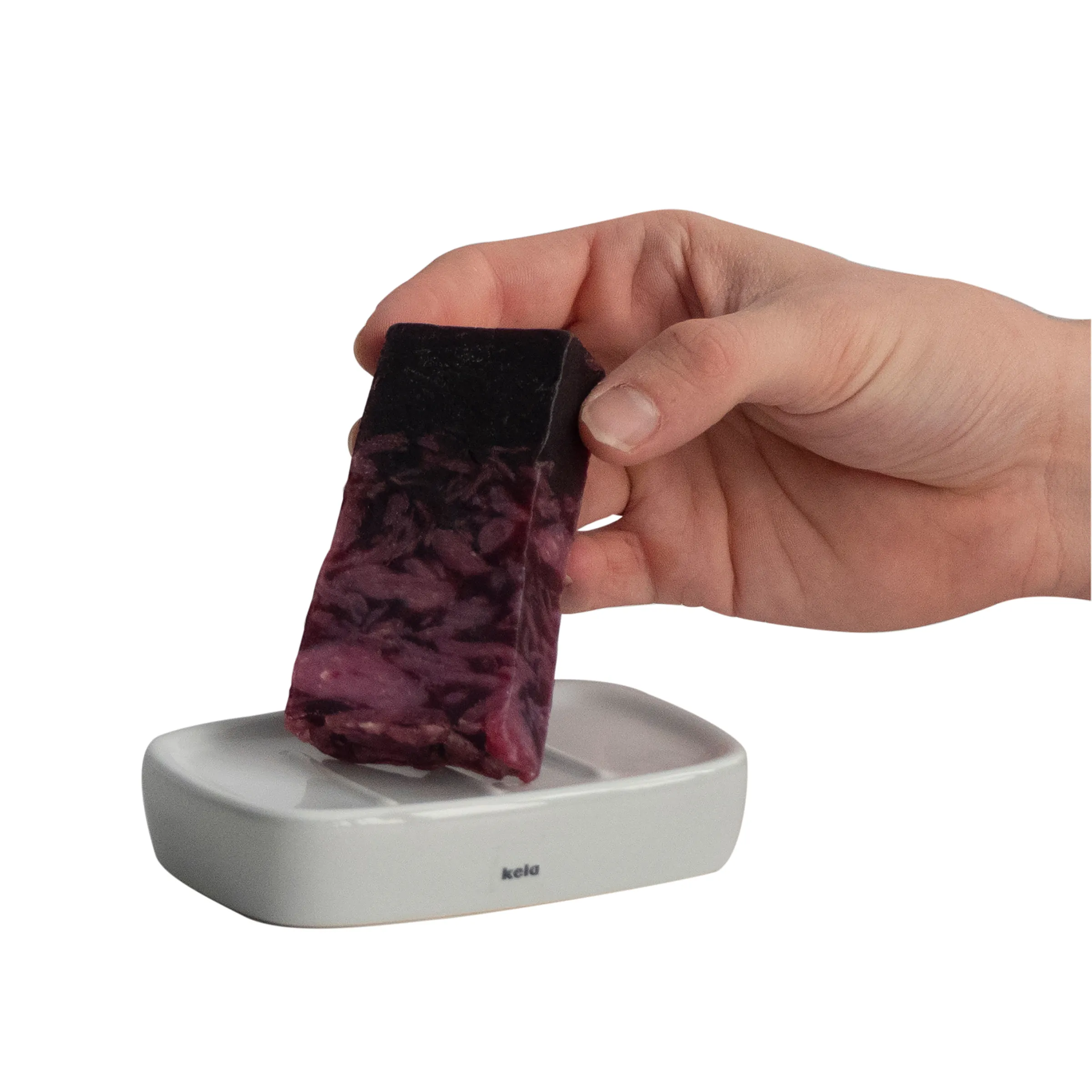 Kelu Seifenschale mit Veloursbeutel - Minimalistische Badaccessoires Hand hält ein dunkelrotes, samtig strukturiertes Tuch über einer weißen Seifenschale mit kelu-Branding
