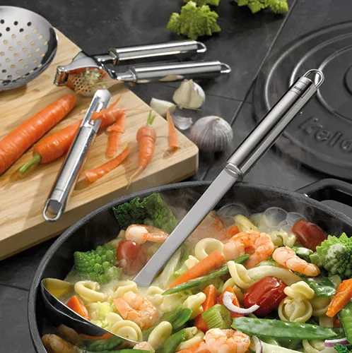 Edelstahl-Küchenhelfer-Set zum Kochen und Gemüse zubereiten Edelstahl-Küchenhelfer-Set beim Kochen mit Gemüsepfanne, geschälten Karotten und Knoblauch