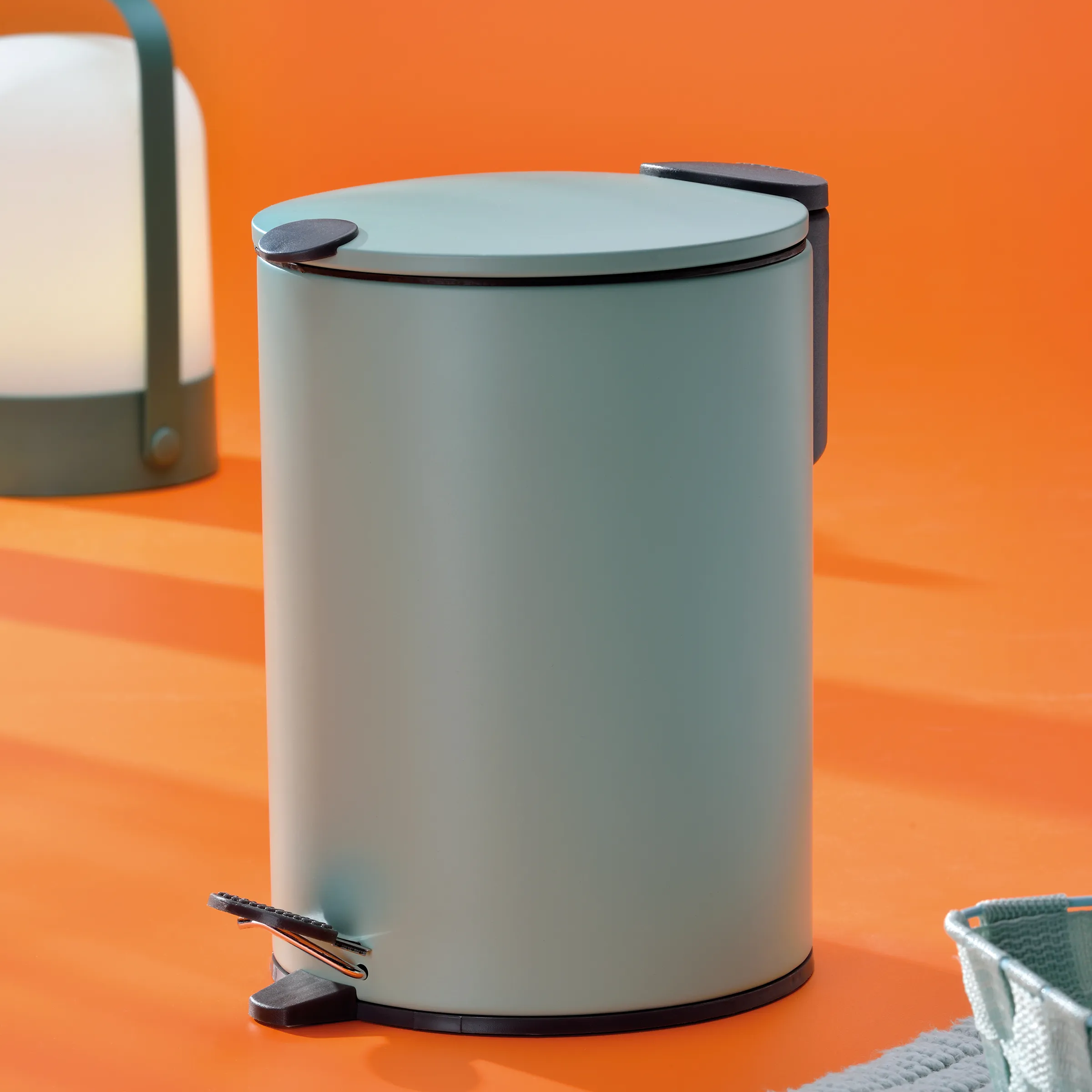 Treteimer grau - moderner Mülleimer mit Pedal Grauer Treteimer mit schwarzem Deckel und Griffen auf orangefarbenem Hintergrund