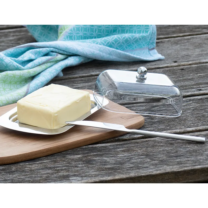 Butterdose mit Glashaube und Edelstahlknopf - Elegante Butteraufbewahrung Butterdose mit Glashaube und Edelstahlknopf, Butterstück auf weißer Schale mit Buttermesser auf Holzbrett