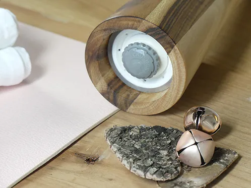 Holzmörser mit Stößel, getrocknete Kräuter und Gewürze auf Holzbrett, daneben Glöckchen