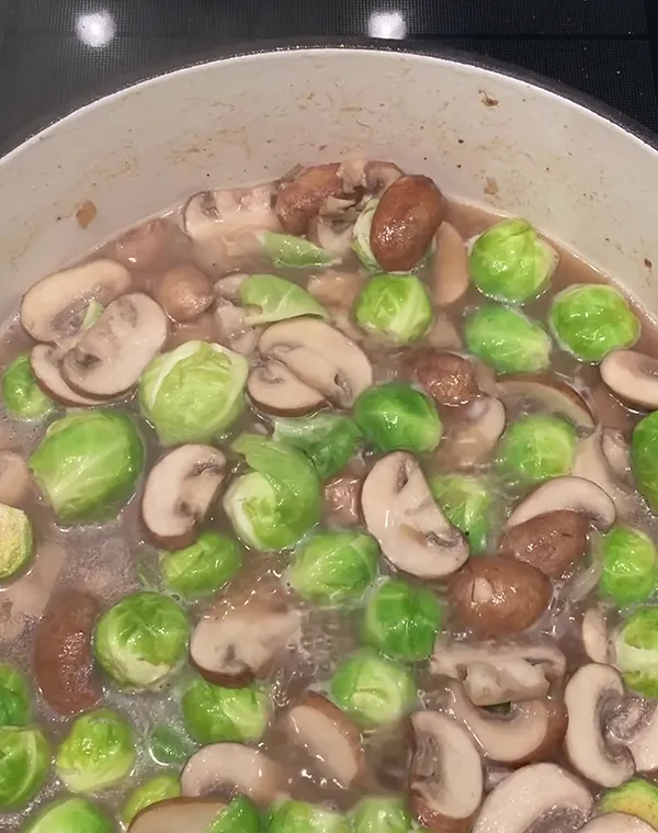 Champignons und Rosenkohl in cremiger Sauce in einem weißen Topf mit braunen Flecken
