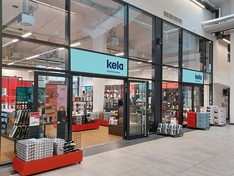 Kela Möbel Store - Moderner Einzelhandelsladen im Einkaufszentrum Kela-Einzelhandelsladen in einem modernen Einkaufszentrum mit großer Glasfassade, roten Elementen und Produktauslagen