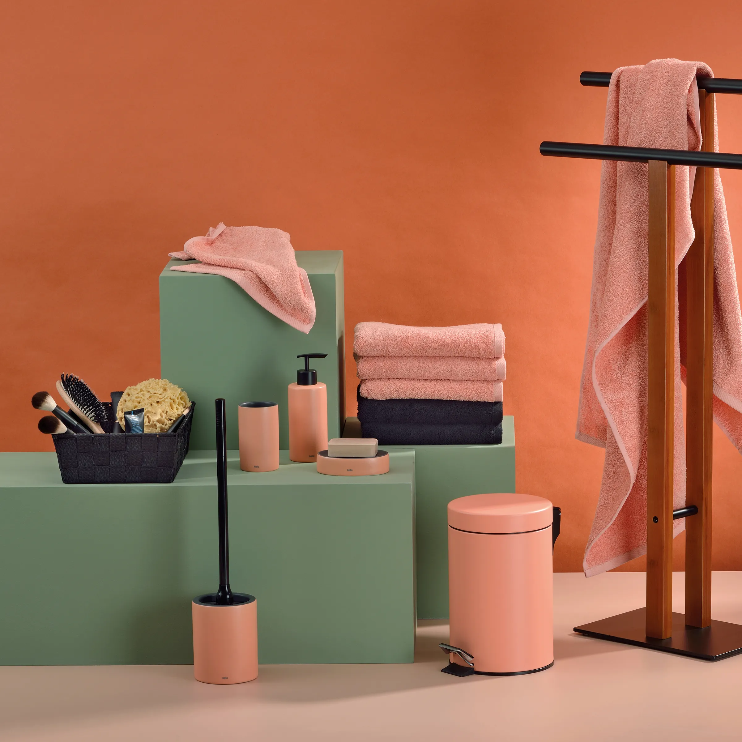Badezimmer Accessoires Set Handtücher Dispenser Badezimmer-Accessoires-Set mit rosa Handtüchern, Pumpenspendern und Behältern auf grünen Podesten vor orangefarbenem Hintergrund