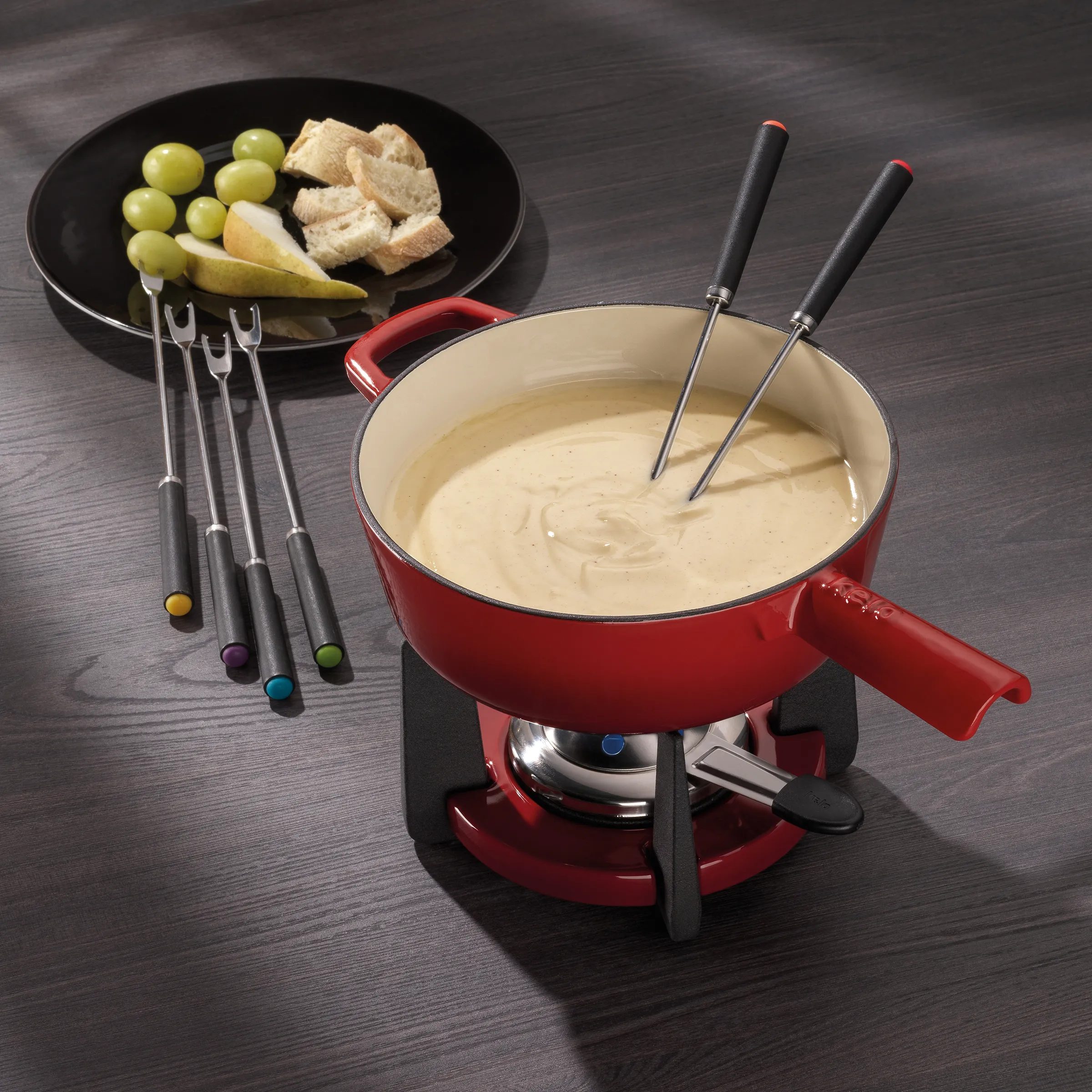 Käse Fondue Set rot - Fondue-Topf mit Zubehör Rotes Fondue-Set mit cremiger Käsesauce in Topf, Gabel-Set und Schwarz-Tablett mit Trauben, Brot und Birne.