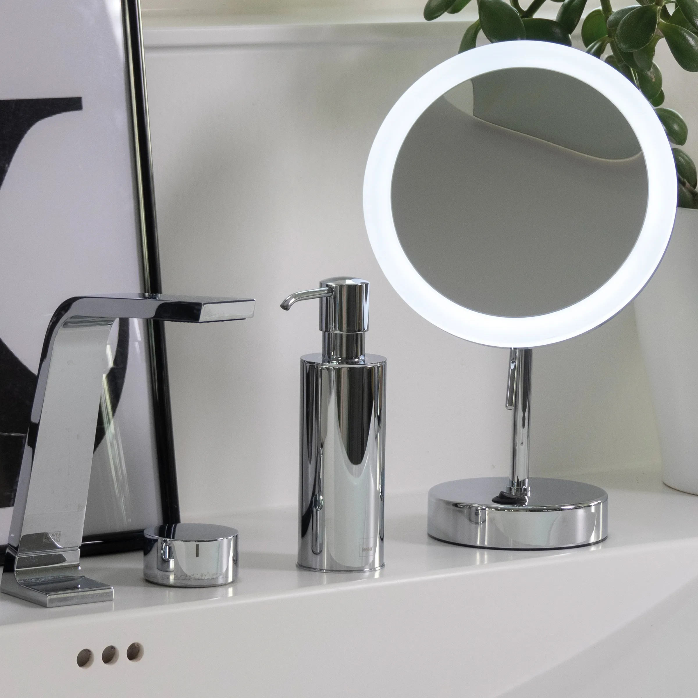 Modernes Badezimmer mit LED-Rundspigel, verchromten Armaturen, Seifenspender und Dekorationen