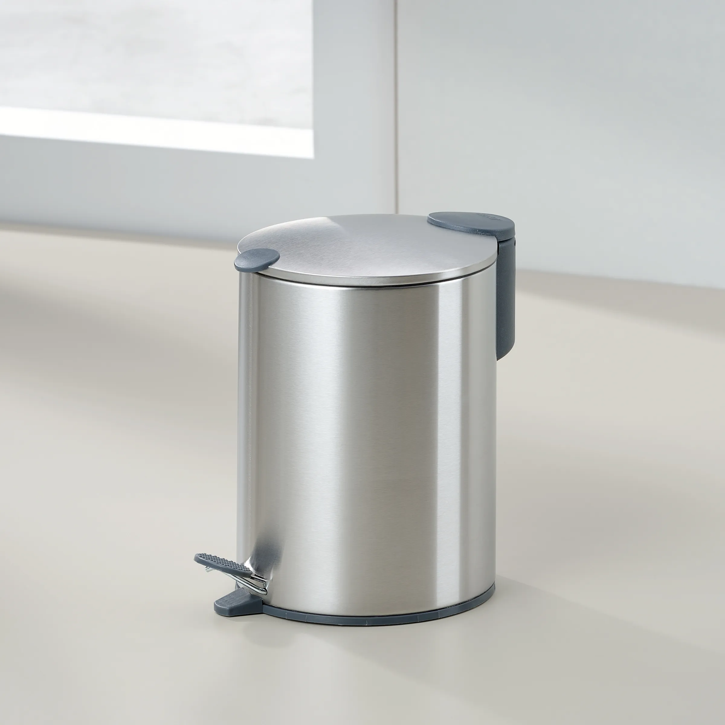 Edelstahl Tretmülleimer mit Pedal-Design Moderner Edelstahl-Tretmülleimer mit silbernem Deckel und anthrazitfarbenen Griffen in minimalistischem Badezimmer