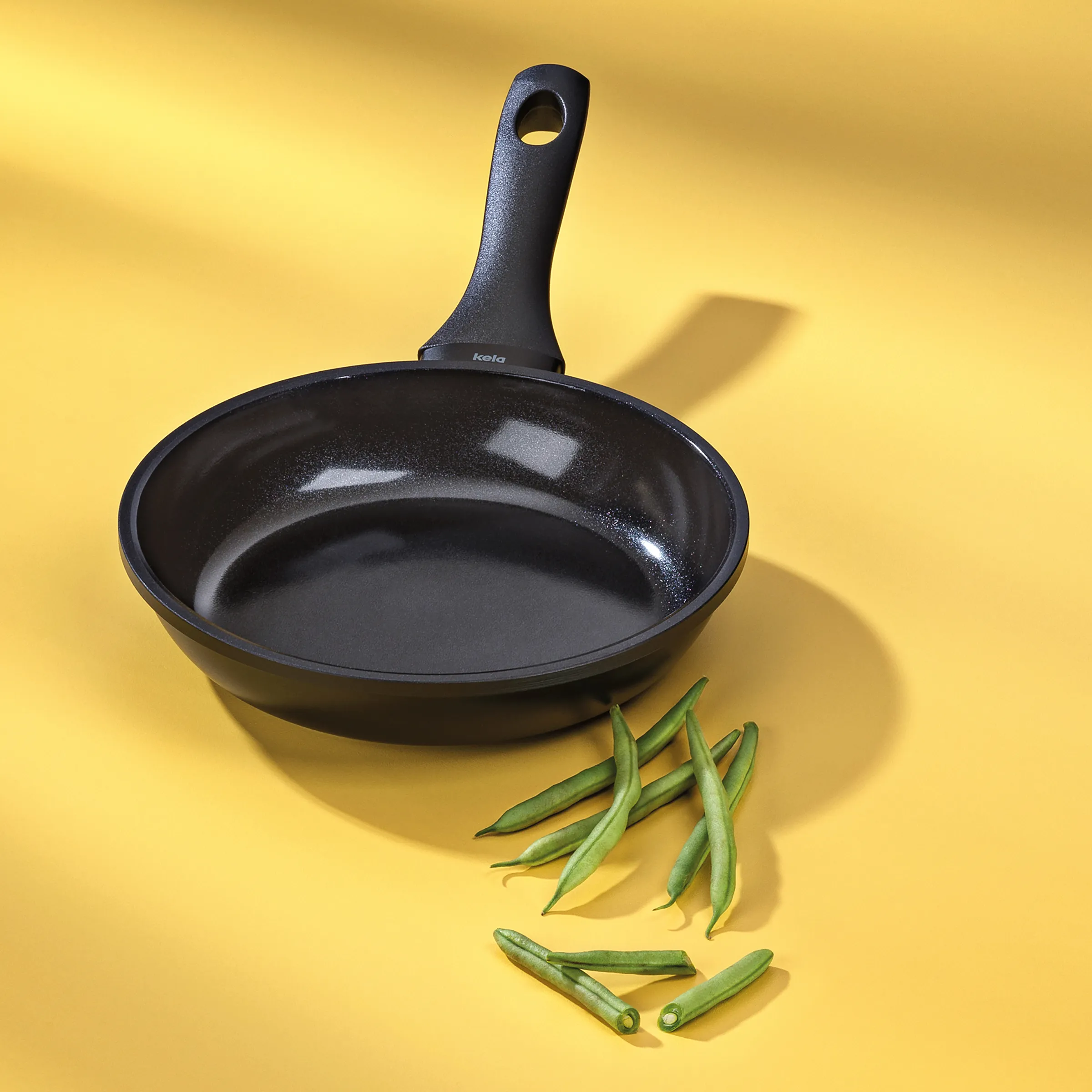 Antihaft-Bratpfanne schwarz - Kochen und Braten Schwarze Antihaft-Bratpfanne mit Metallgriff und grünen Bohnen auf gelbem Hintergrund