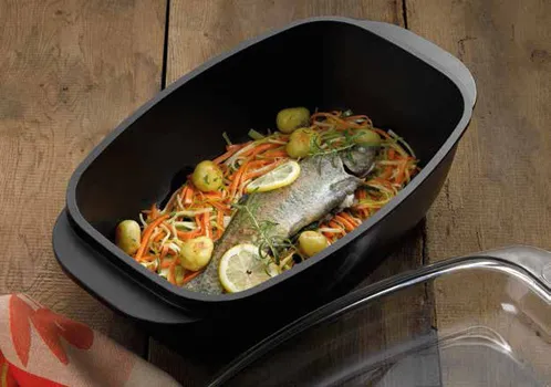 Fisch in Bratform mit Gemüse zubereiten - Ofenform für Fischgerichte Ganzer Fisch mit Gemüse und Zitronenscheiben in schwarzer rechteckiger Bratform auf Holztisch