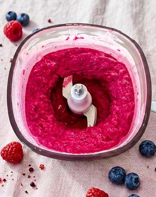 Himbeerpüree selber machen - Mixer mit Beerenpüree Himbeerpüree in Mixer mit Himbeeren und Blaubeeren auf Holzoberfläche