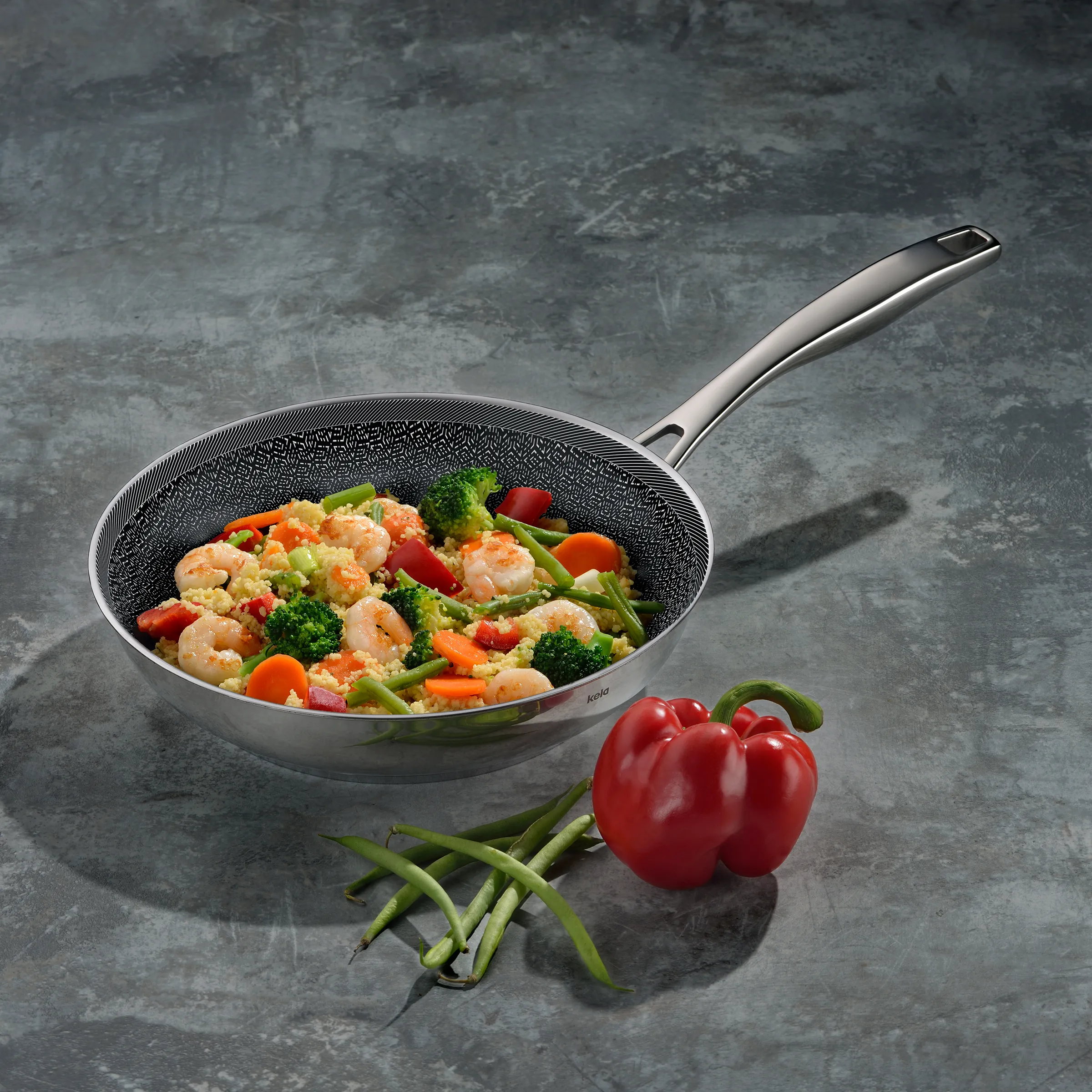 Wok mit Garnelen, Gemüse und Reis auf grauem Untergrund, daneben rote Paprika und grüne Bohnen